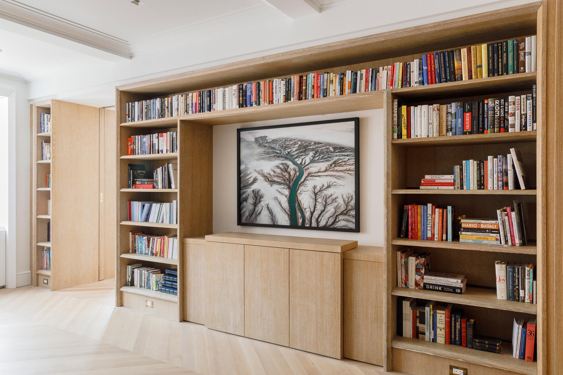 A custom-designed bookshelf surrounds artwork and cabinetry. Within the cabinetry, there's a TV on a concealed motorized lift, and above is photography by Edward Burtynsky