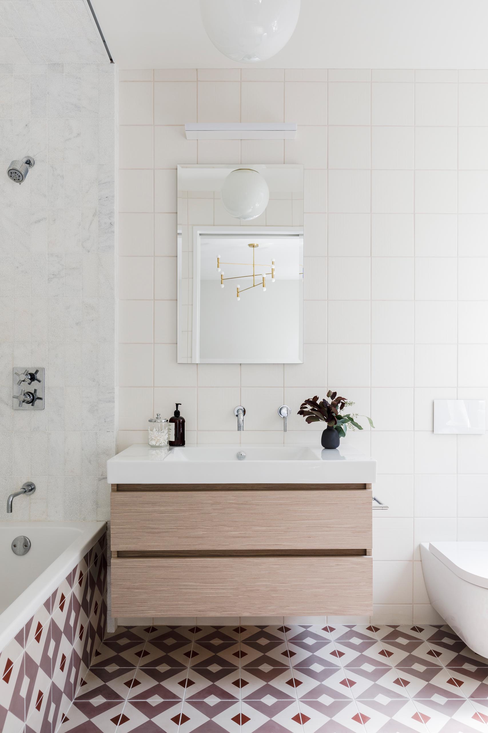 In this kid's bathroom, there's a floating wood vanity, while patterned tiles cover the floor and plain square tiles cover the walls.