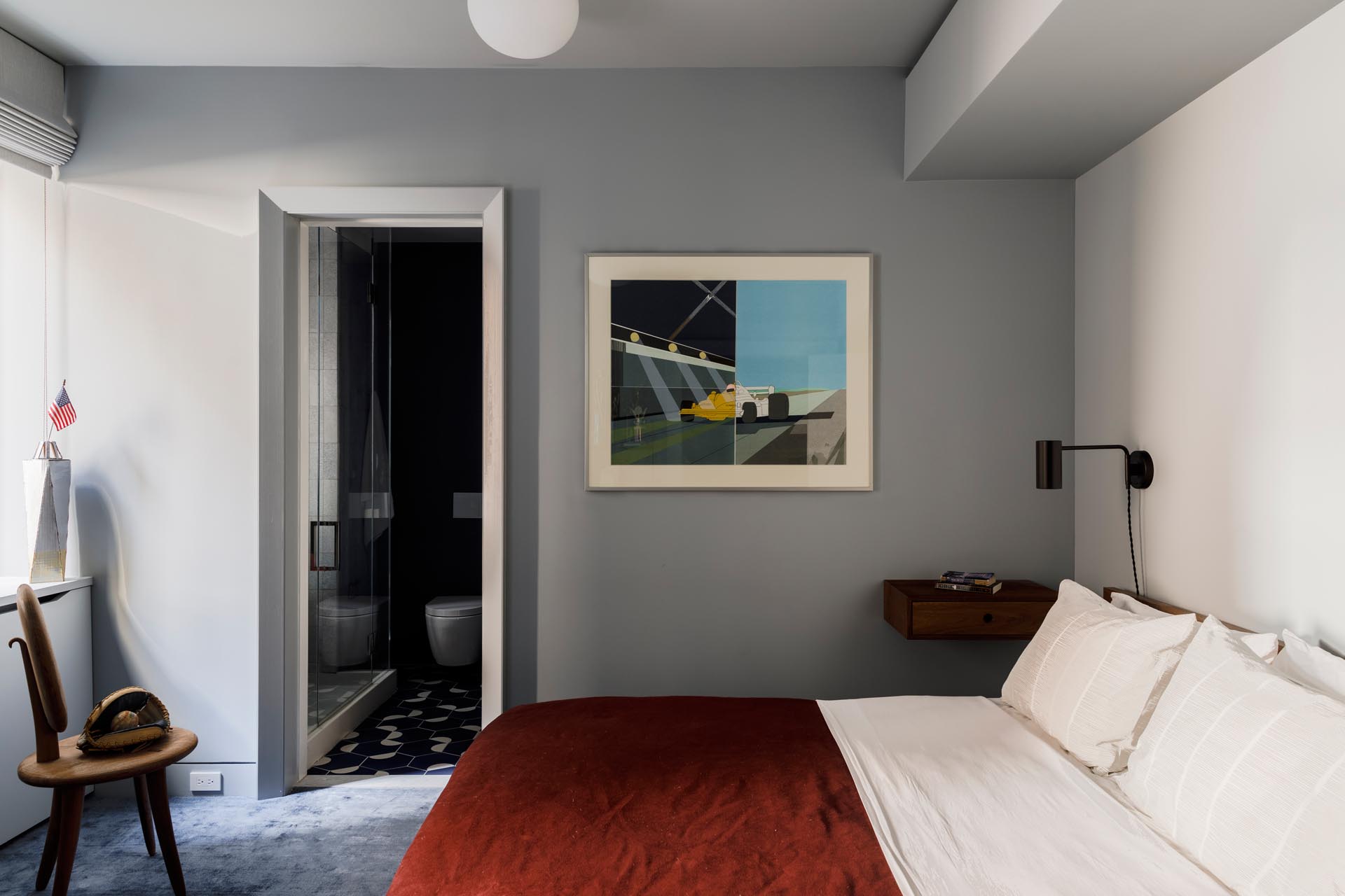 In this guest bedroom there's a contemporary color palette with gray walls, white trim, and a deep burnt orange bedspread.