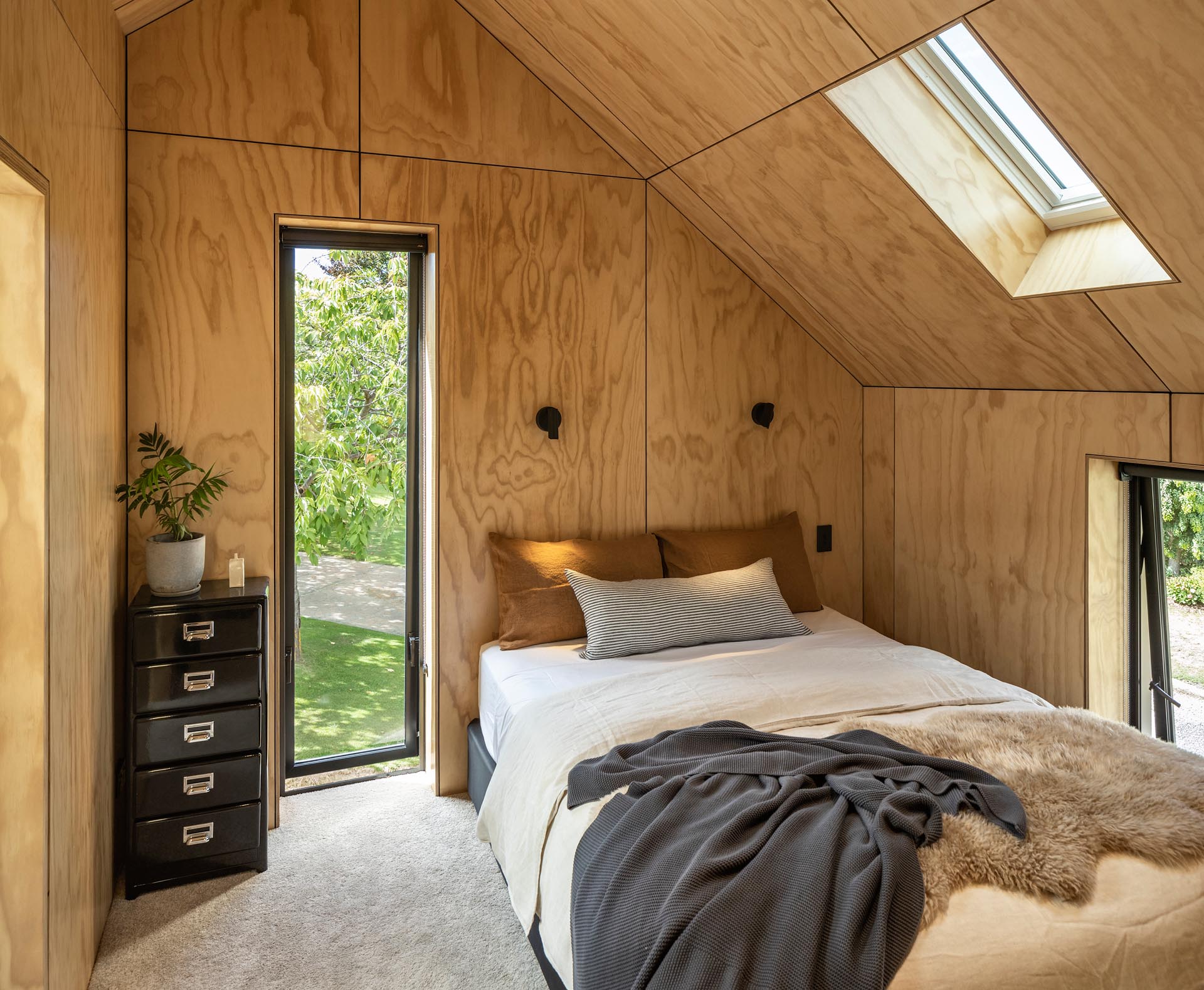 In this modern bedroom, a tall window provides views of the trees, while the wood walls and ceiling adds a warm and cozy touch.