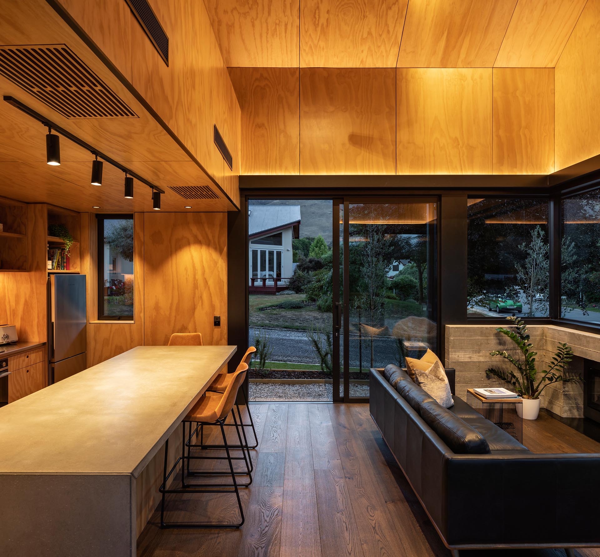 The lower floor of this small home contains a double-height living and kitchen space, with hidden lighting that highlights the wood ceiling. 
