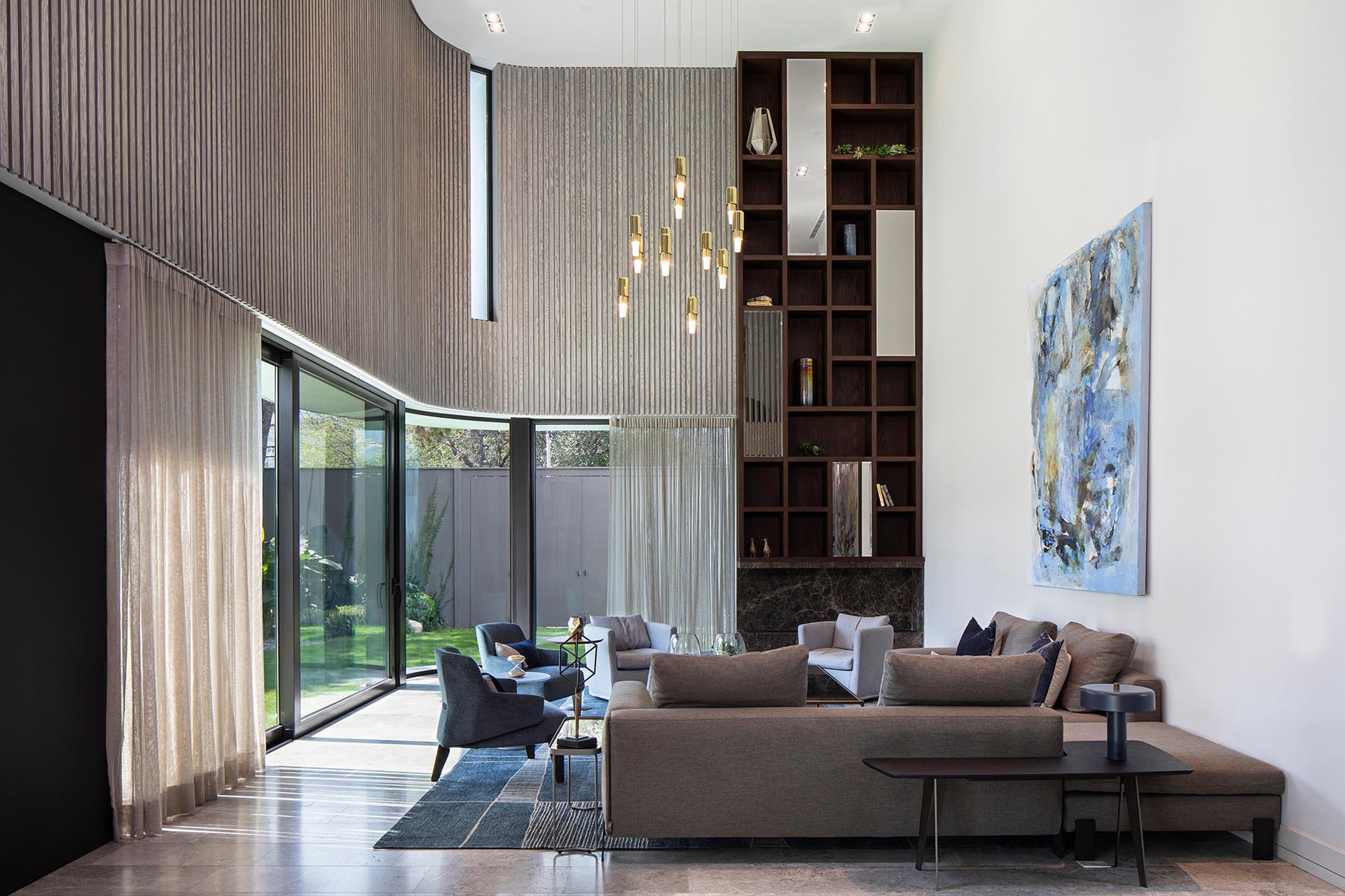 This modern living room opens up to the backyard via two large sliding glass doors that retract into a hidden pocket. Vertical wood paneling echoes the pattern of the exterior pipe screen.