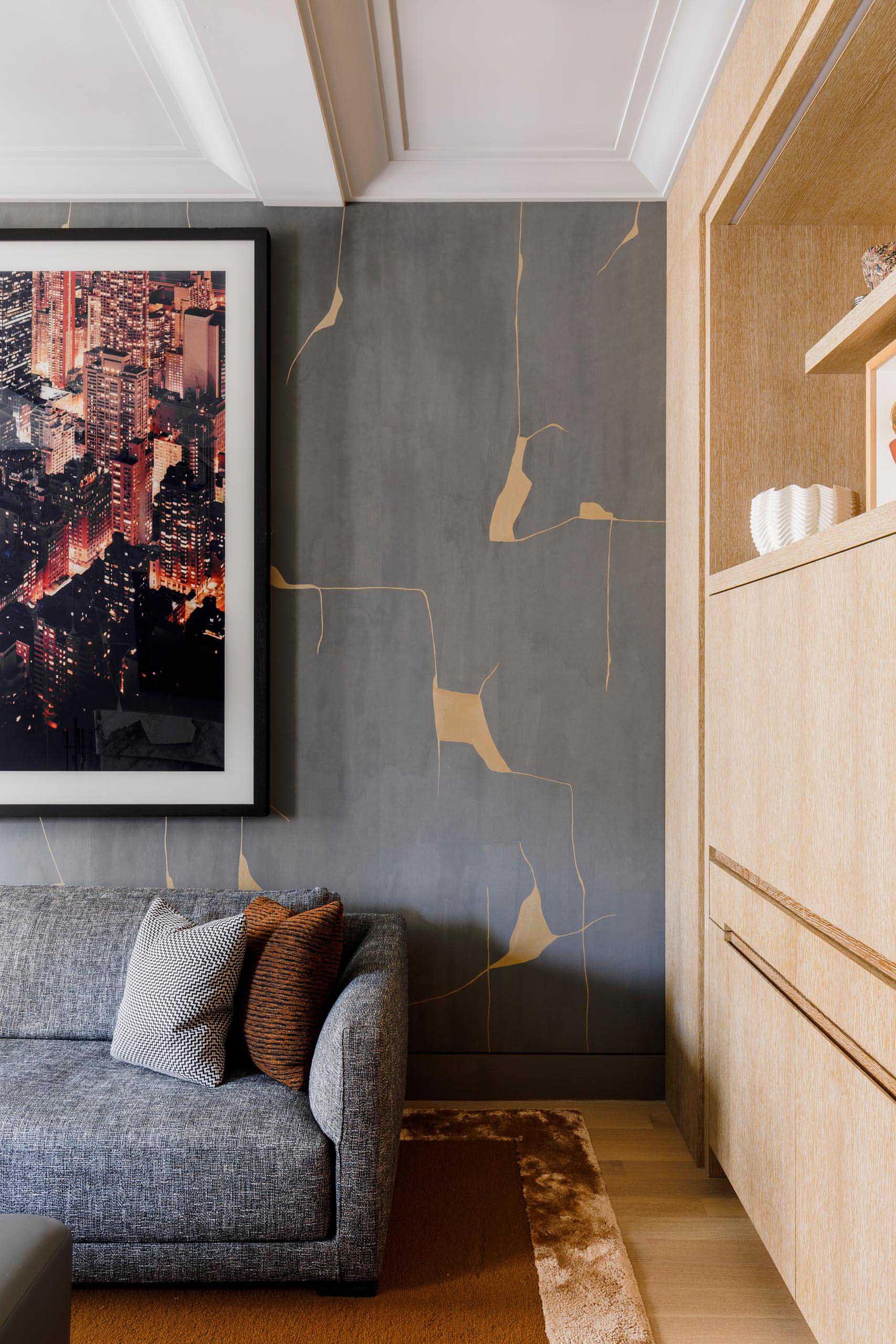 In this modern media room, there's hand painted “Kintsugi” wallcovering by Porter Teleo, a Patagonia marble fireplace, a custom leather, walnut and glass ottoman by MKCA and fabricated by Manzanares Furniture, a sofa by Poliform, and an overhead “Maxihedron” pendant by Bec Brittain for Roll and Hill.