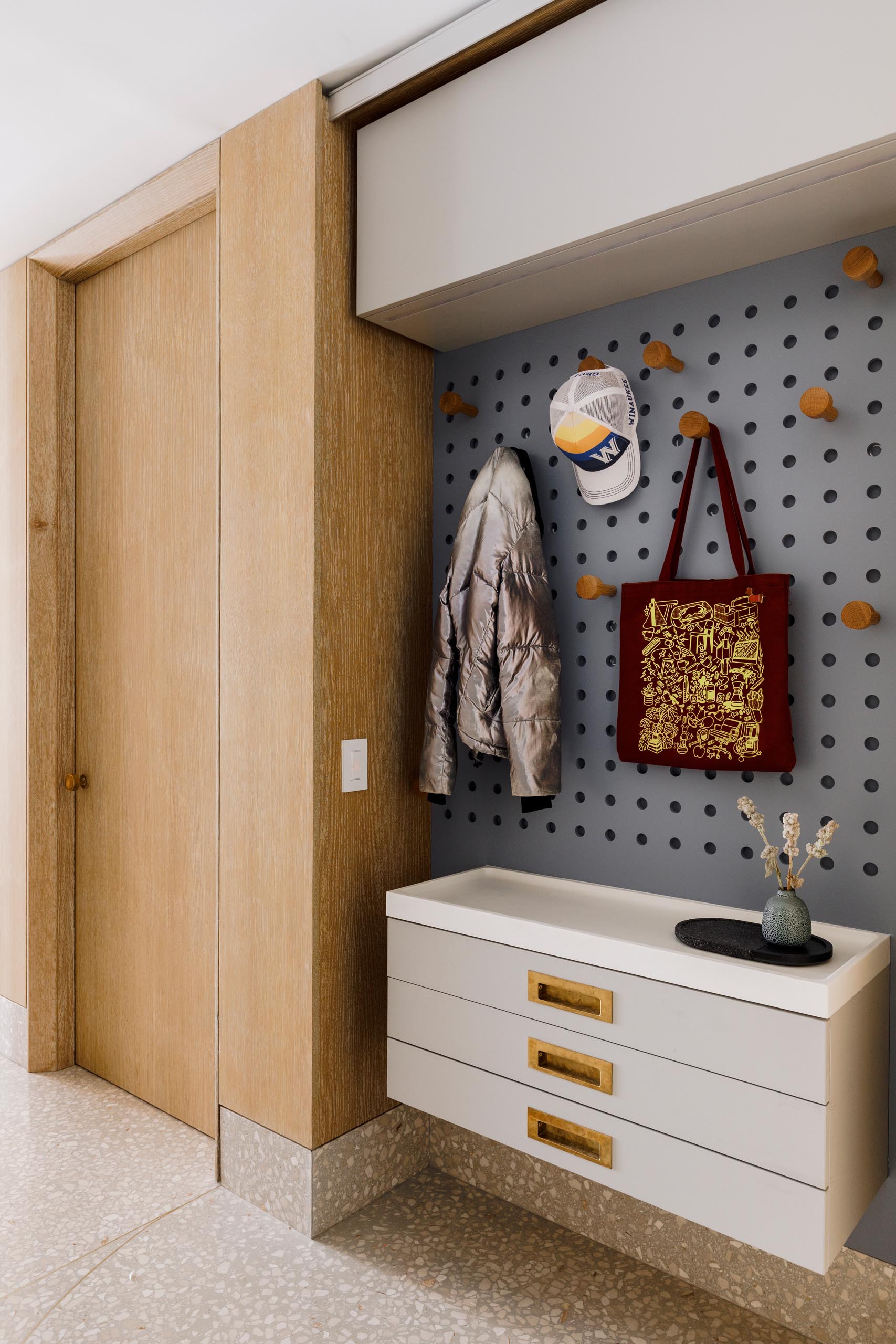 In this modern mudroom, there's a floating cabinet and a pegboard wall for storage.