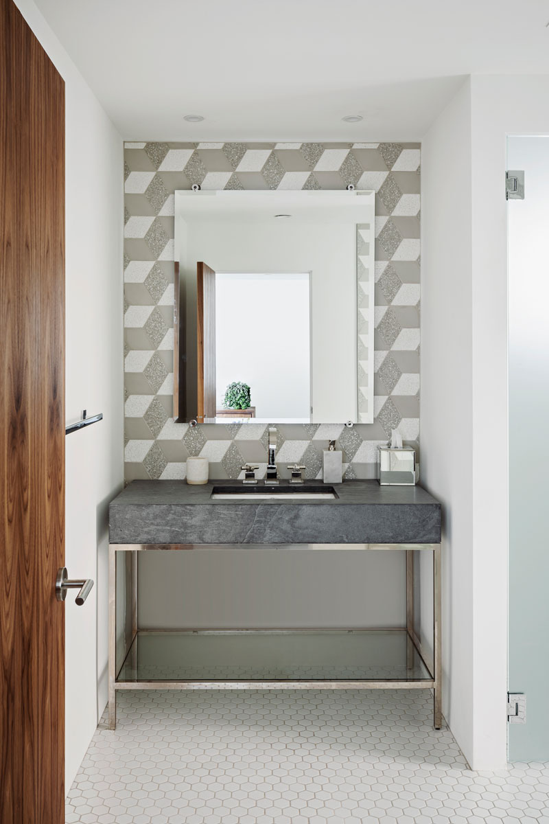 In the powder room of a remodeled house by The Ranch Mine, decorative geometric tiles cover the wall, while a simple vanity with chrome accents adds a touch of glamour.