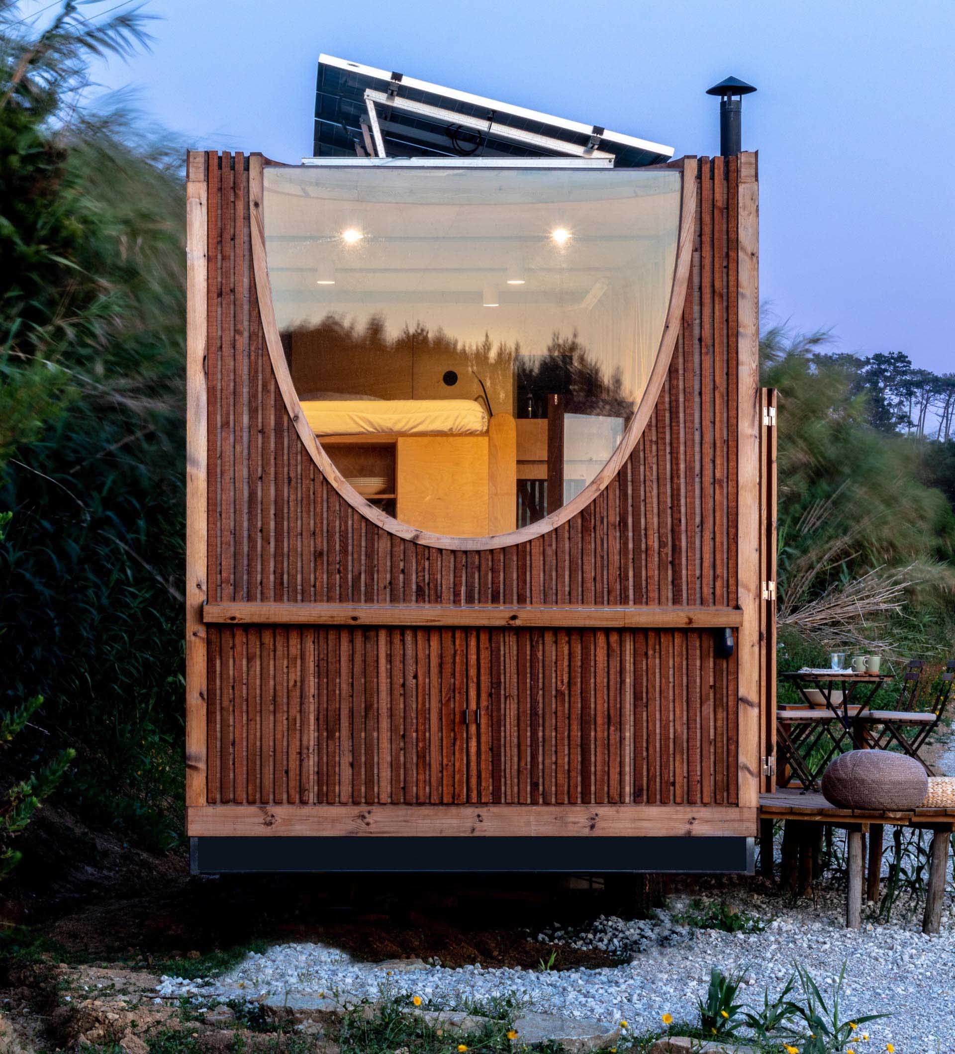 A modern tiny house covered in heat-treated timber, has a birch plywood interior, kitchen, bathroom, and two sleeping areas.