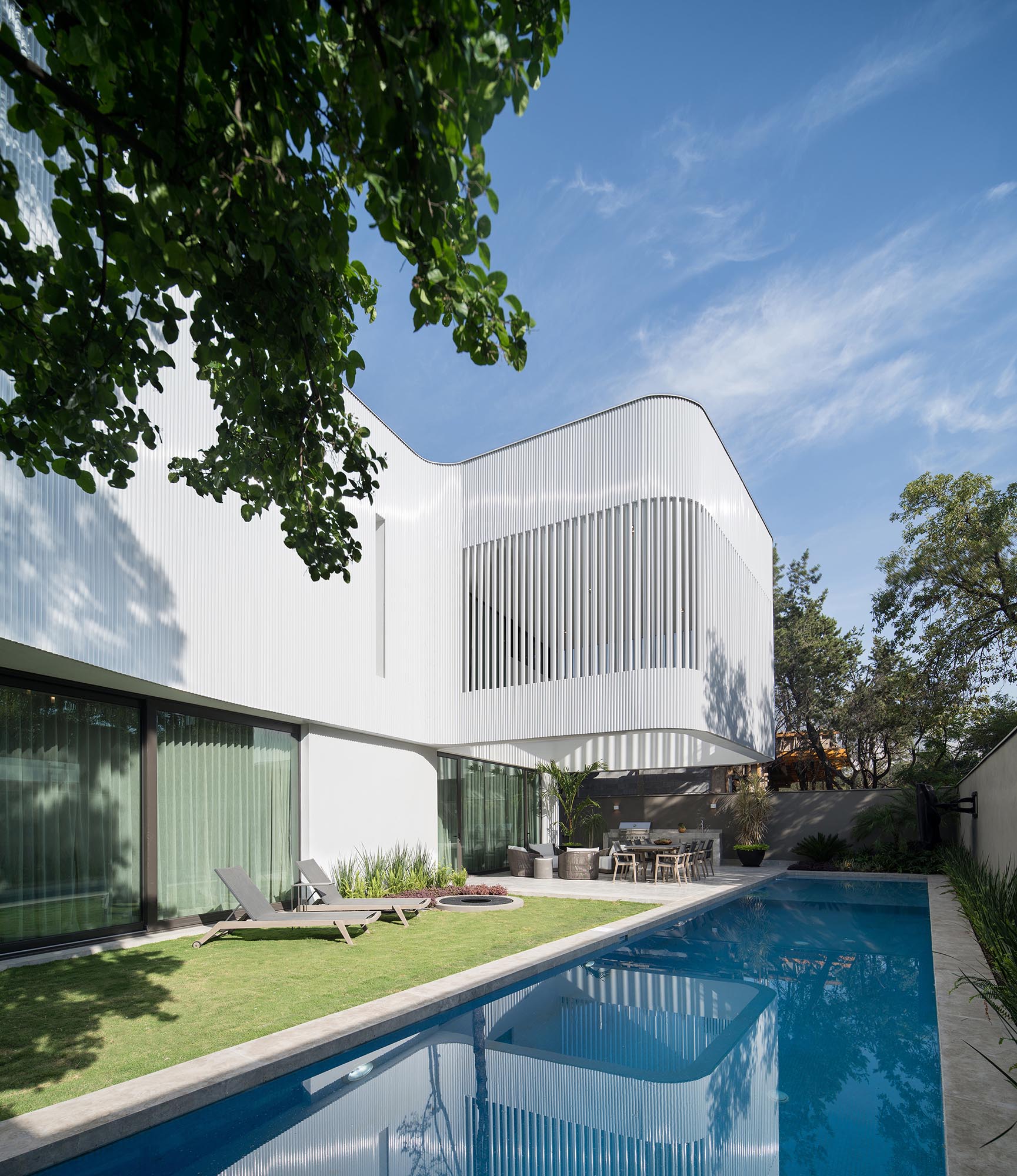 The white screen made from metal pipes, is contrasted by the dark bronze finish of the window frames, sliding garage doors, and pivoting front door.