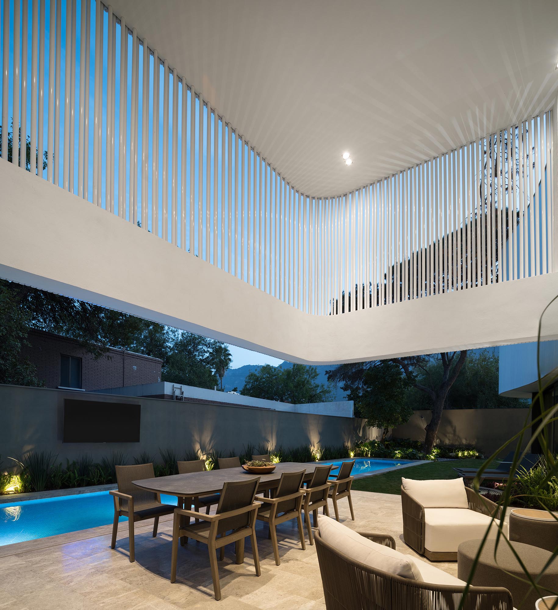 A cantilevered concrete ribbon wrapped in pipes provides shade to an outdoor seating and dining area.