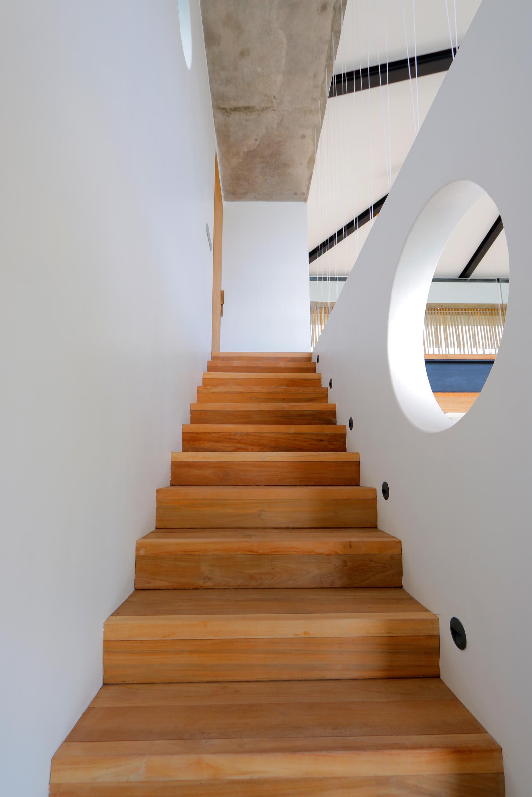 A modern beach house with wood stairs that connect to the upper level of the home.