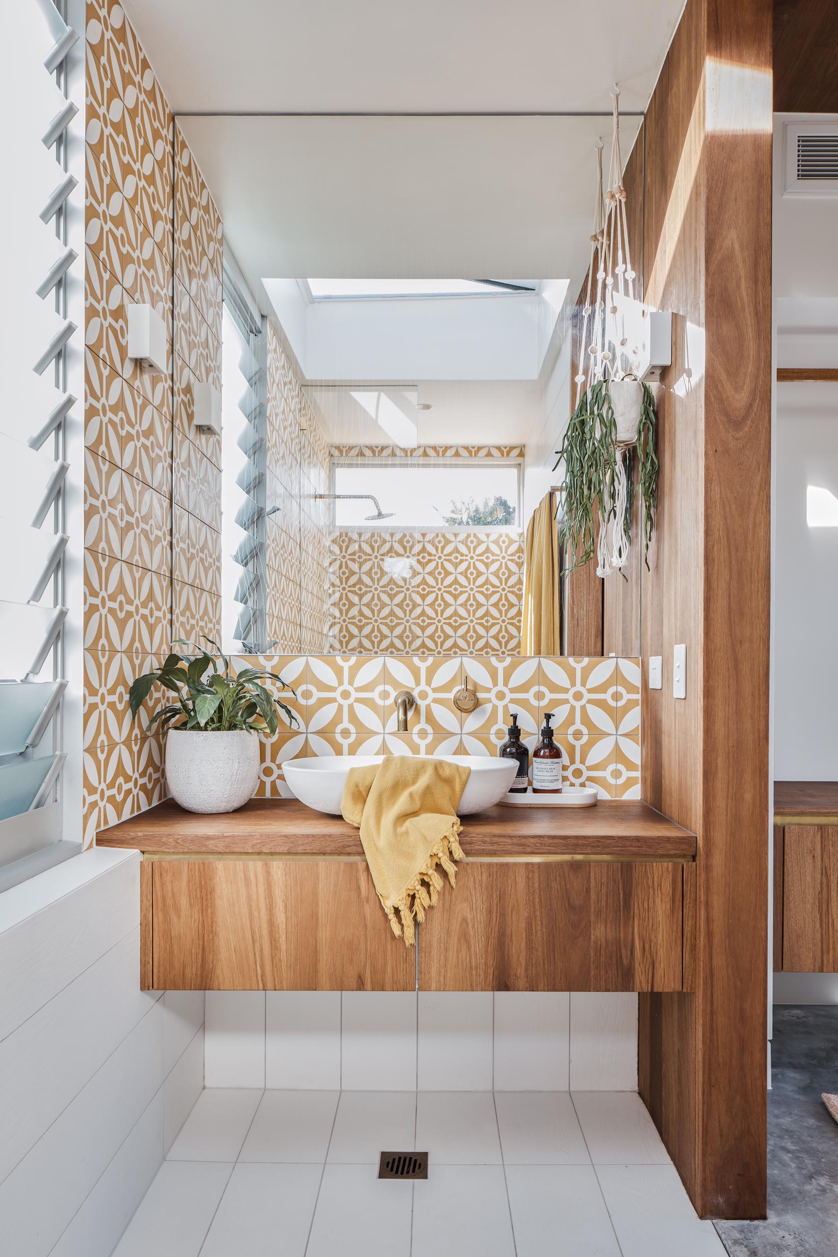 This modern en-suite bathroom includes patterned tiles, a warm wood vanity, and a walk-in shower.