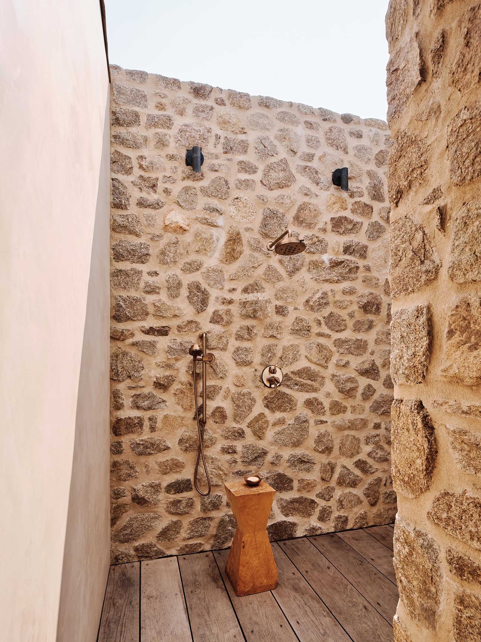 An outdoor shower with stone walls and wood flooring.