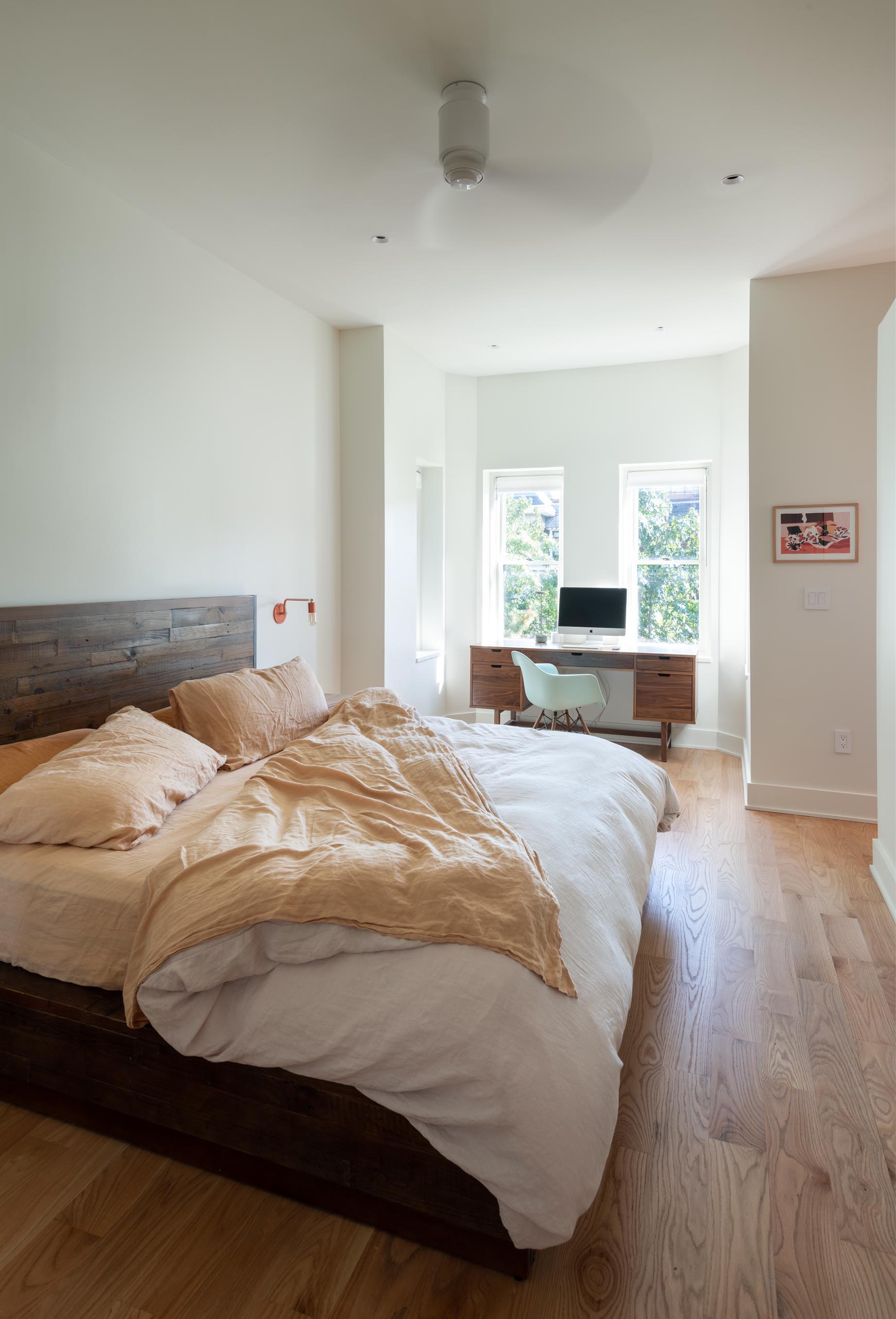 A bright bedroom with high ceilings and a home office by the windows.