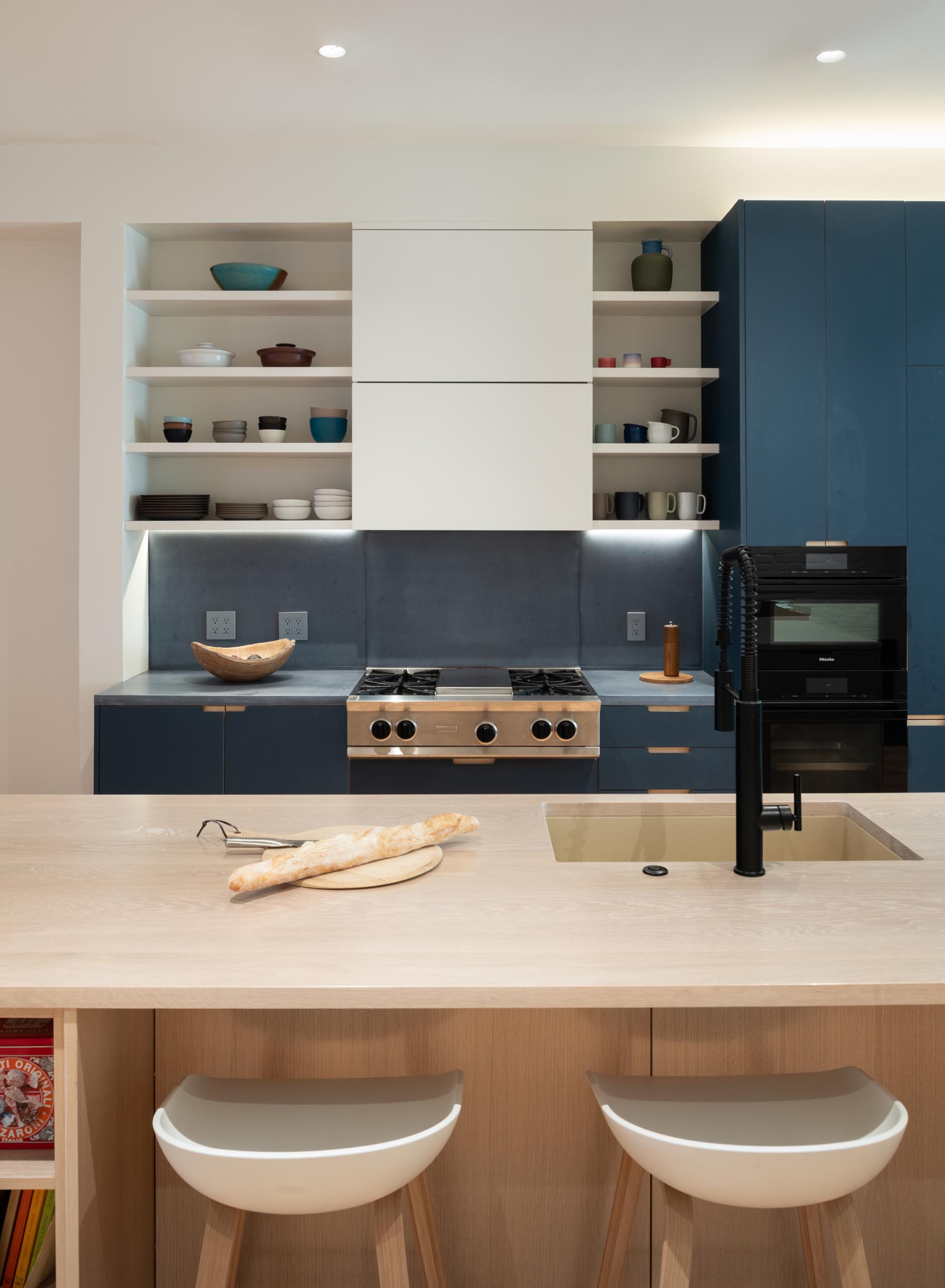 This modern kitchen includes blue and white cabinets, gray countertops and backsplash, and a wood island with seating.