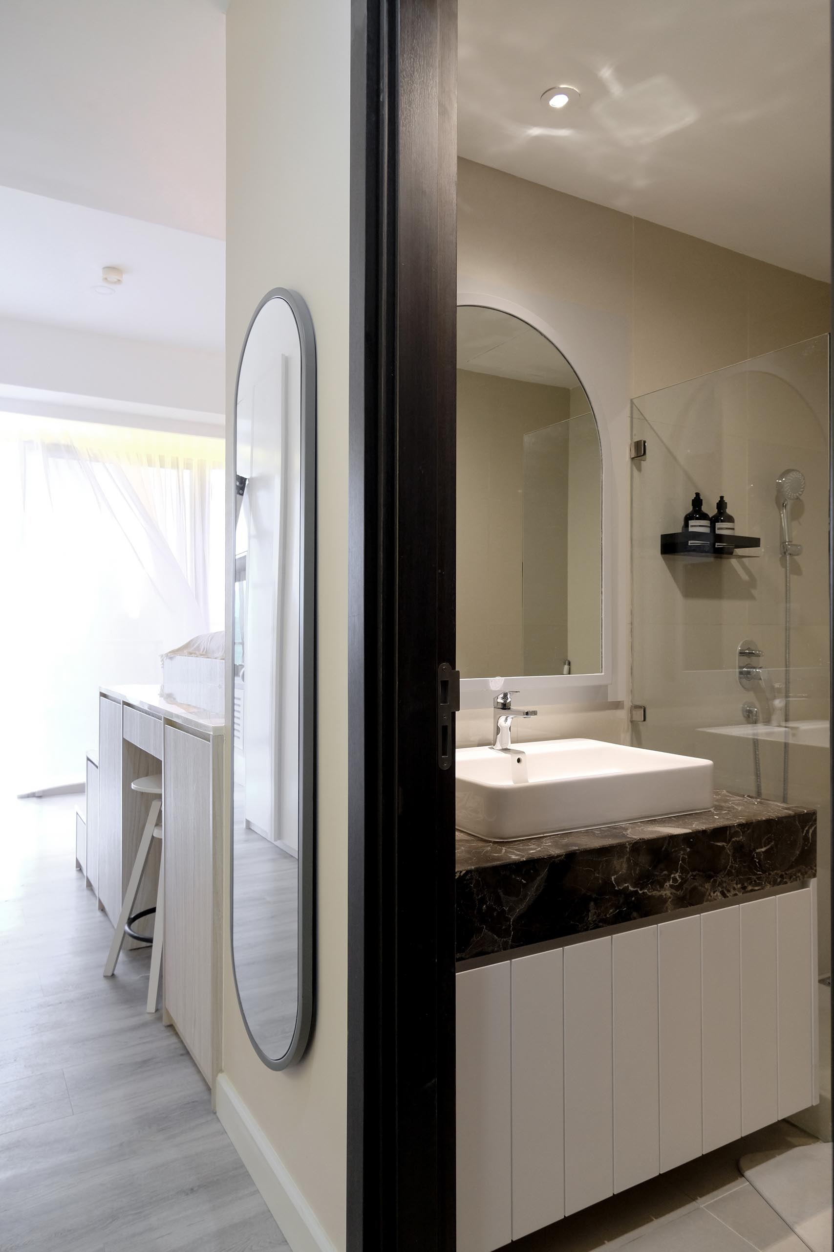 This small bathroom, which is located by the front door, has a modern vanity, a walk-in shower, and an arched mirror which matches the wall mirror in the hallway.