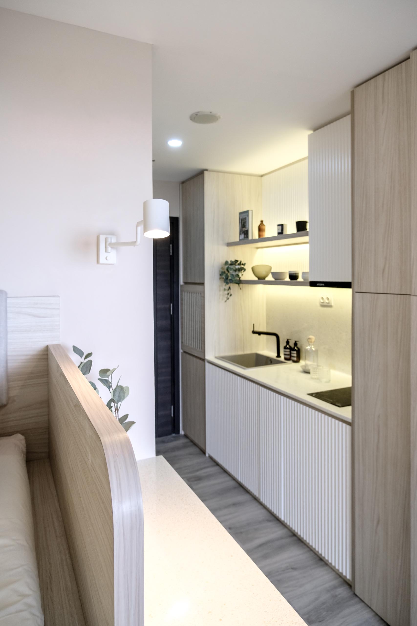 The kitchen of a small apartment includes textured cabinet fronts that help to define the kitchen area, while added lighting underneath the shelves helps brighten the countertops.