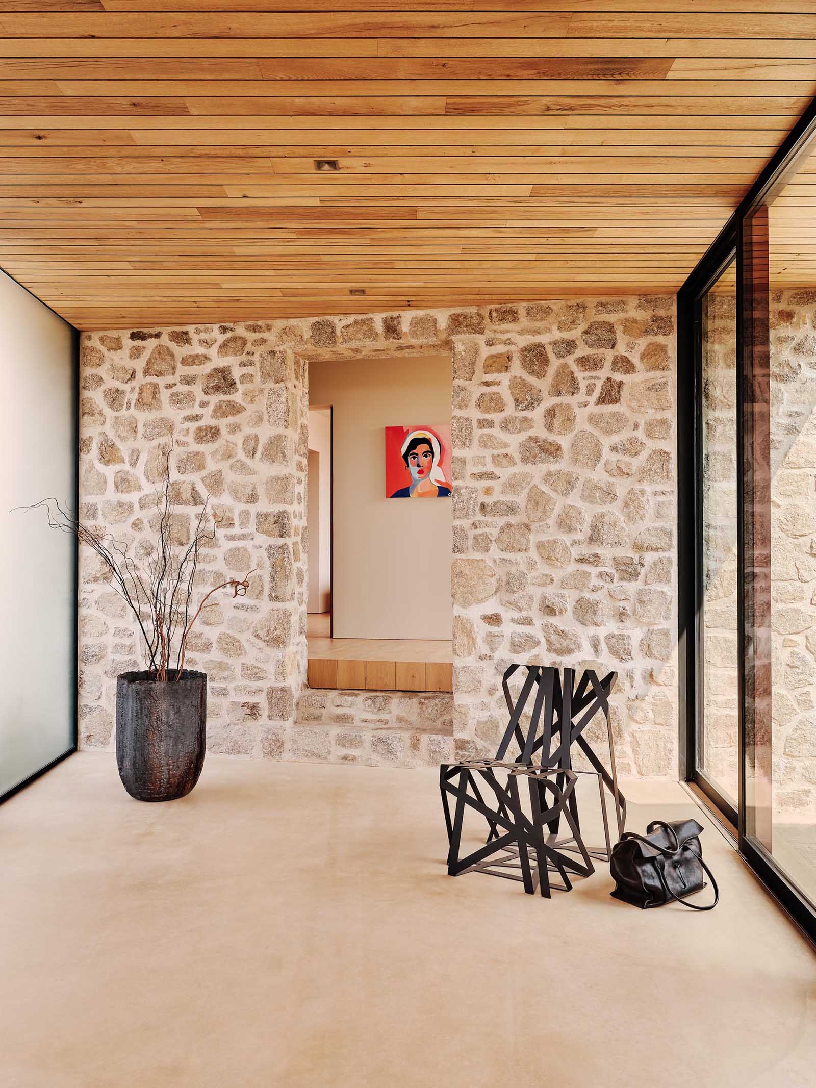 A modern house with stone walls, floor-to-ceiling windows, and wood ceiling.