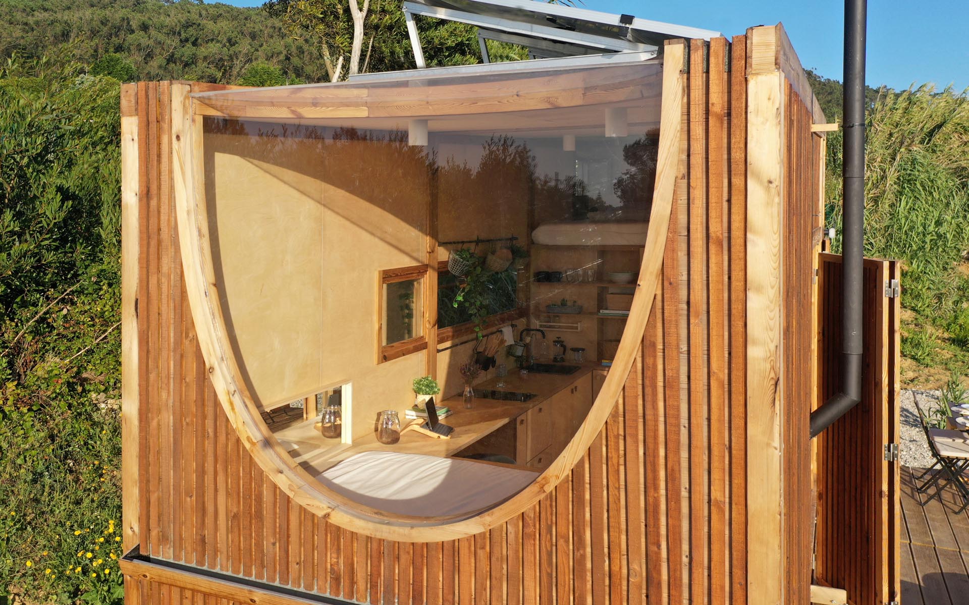 A modern tiny house covered in heat-treated timber, has a birch plywood interior, kitchen, bathroom, and two sleeping areas.