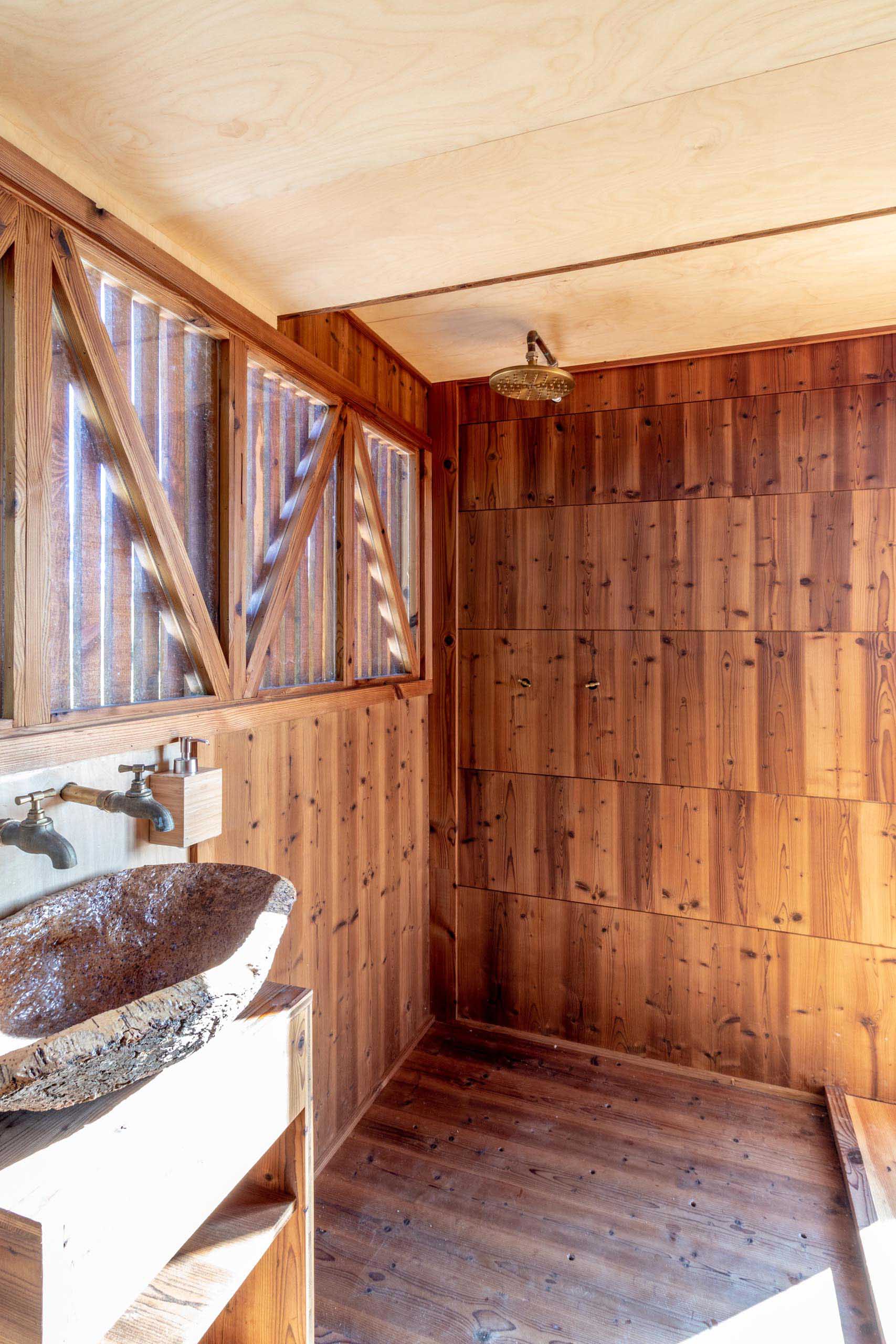 This wood-lined tiny house bathroom is located underneath the sleeping loft, and includes windows, a shower, and a vanity area.