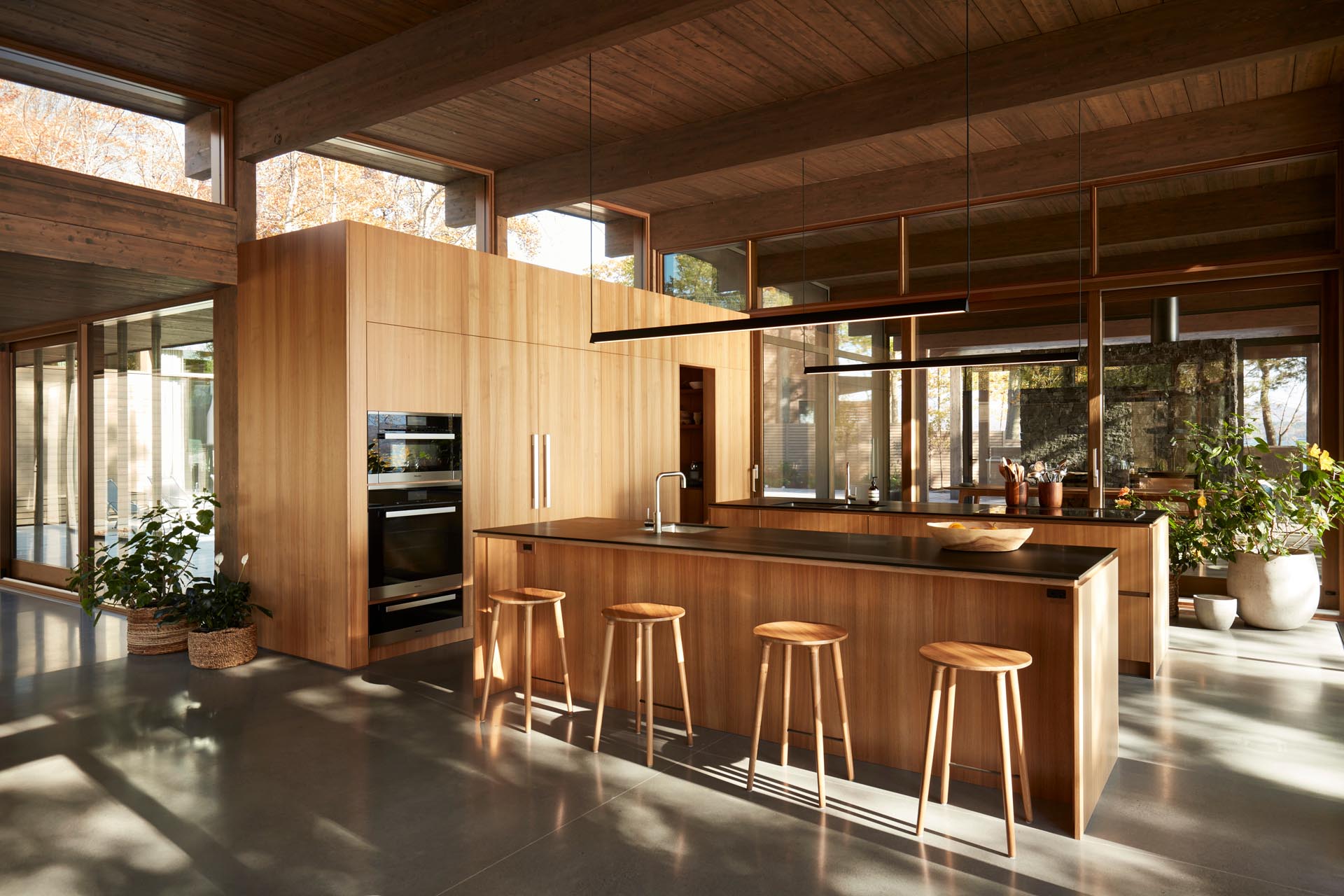 This modern kitchen with two islands also includes flat paneled walnut cabinetry, open shelving, black Fenix NTM countertops, and concrete flooring.