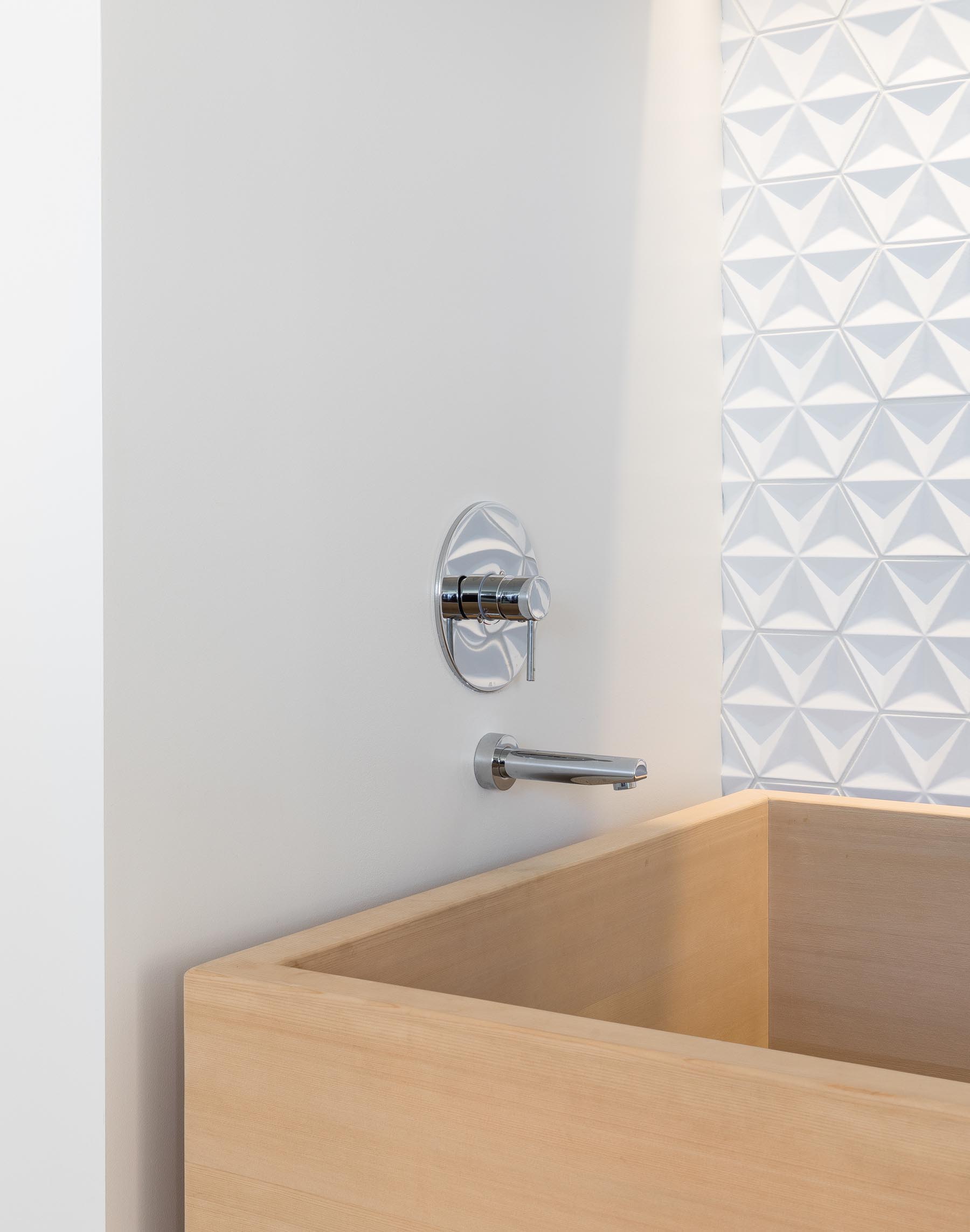 A contemporary master bathroom featuring textured tiles, a wood vanity, and a deep wood soaking tub.