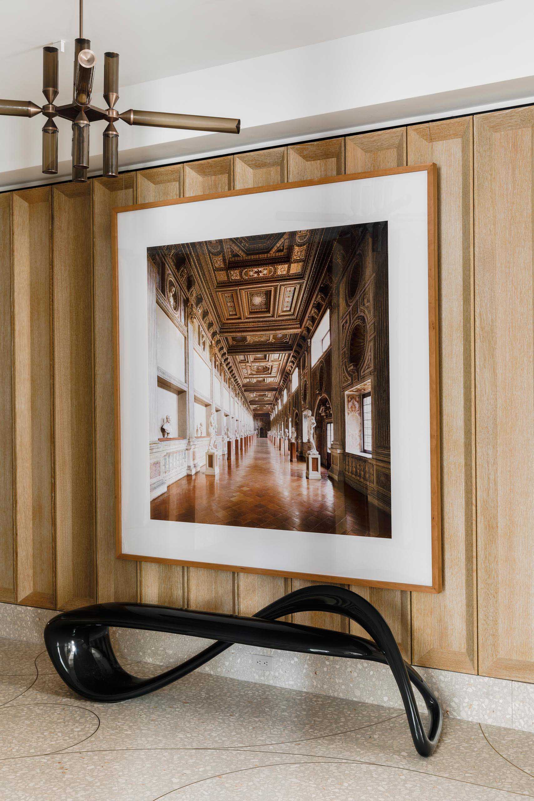 This entryway and gallery includes deep coffered paneling in cerused white oak, custom terrazzo floor with hand bent brass inlay, two “Castle” pendants by Jason Miller for Roll and Hill, photo artwork by Candida Hofer, and a fiberglass bench by Brodie Neill.