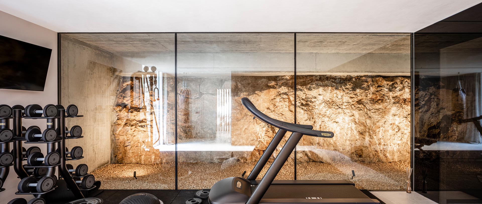 A modern home gym with a unique feature of floor-to-ceiling glass walls that provide views of the natural rock found on the homes building site.
