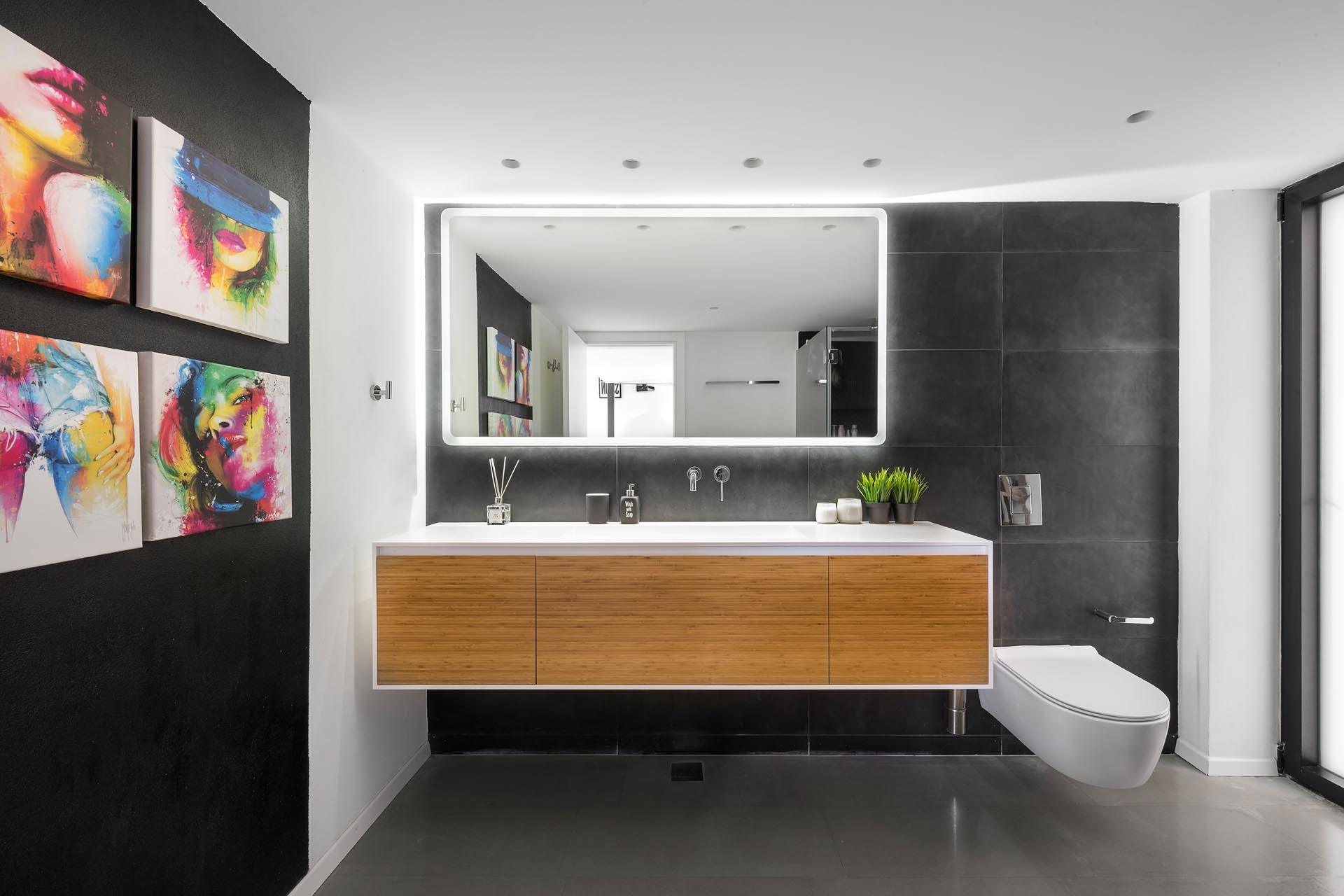 A modern bathroom with black accent wall, large gray tiles, a floating vanity, and a mirror with LED lighting.