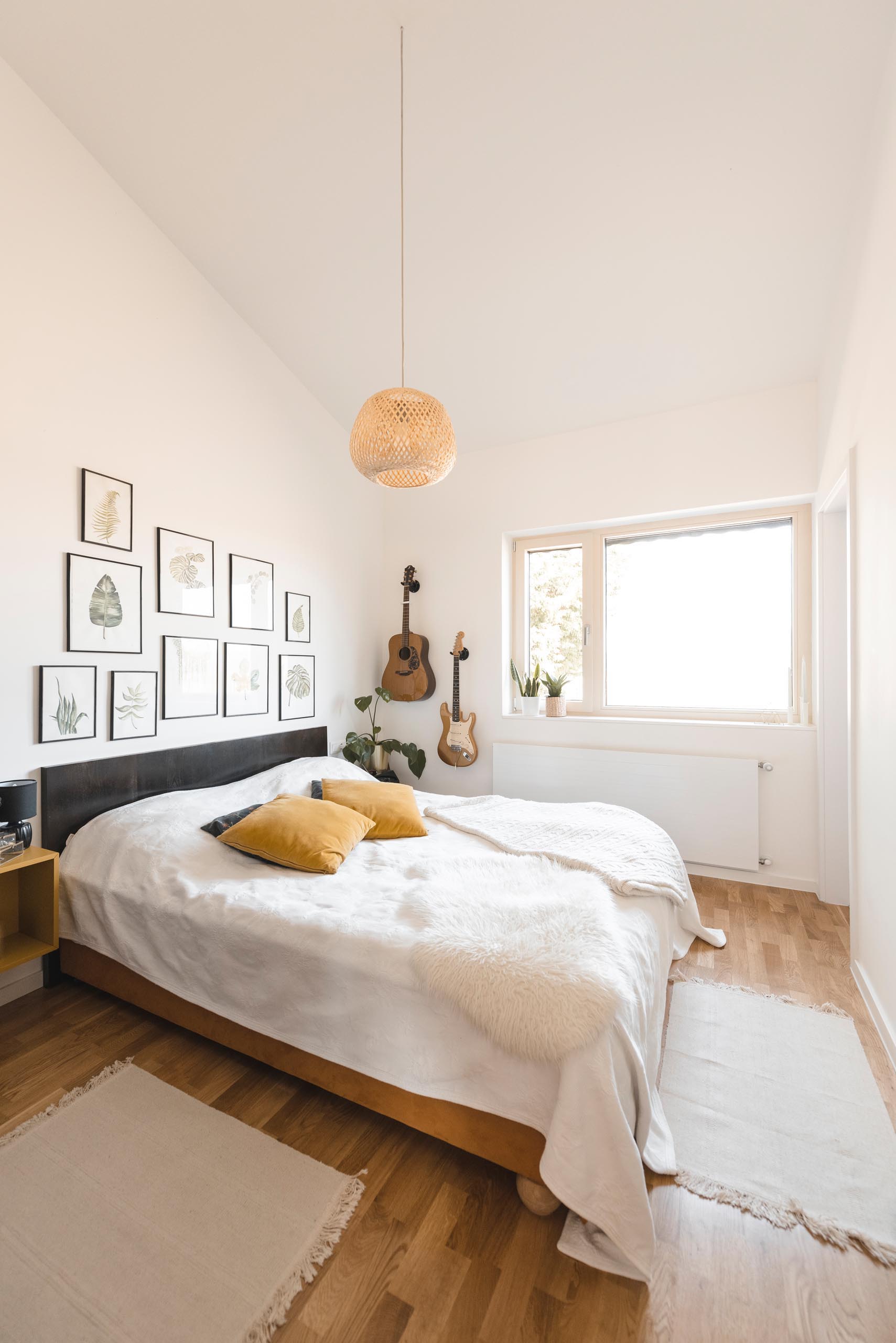 A modern bedroom with minimal furnishings and botanical artwork above the headboard.