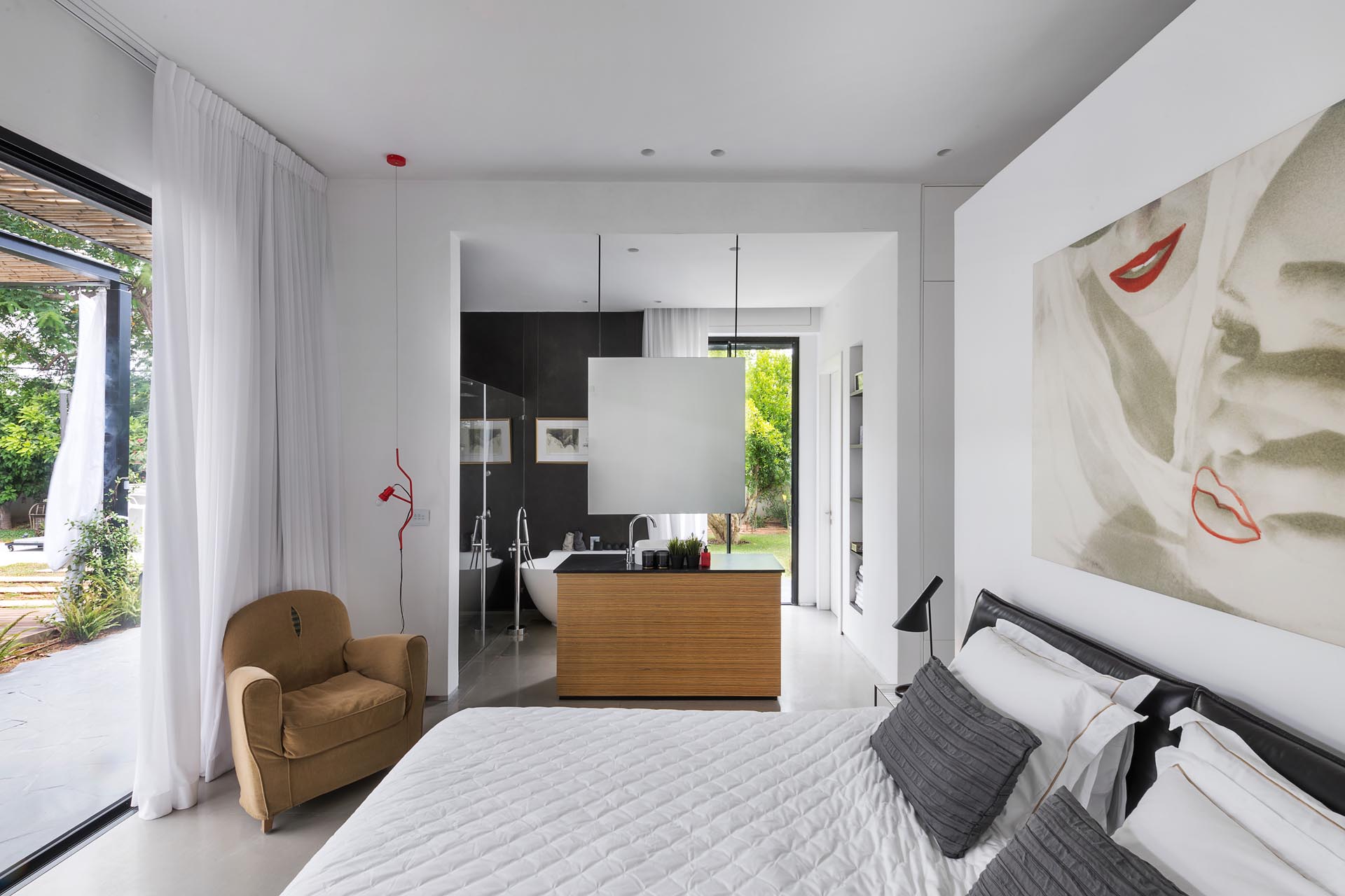 This modern master bedroom also opens to the outdoor spaces and has an en-suite bathroom with a freestanding bathtub, a black accent wall, and a glass-enclosed shower.