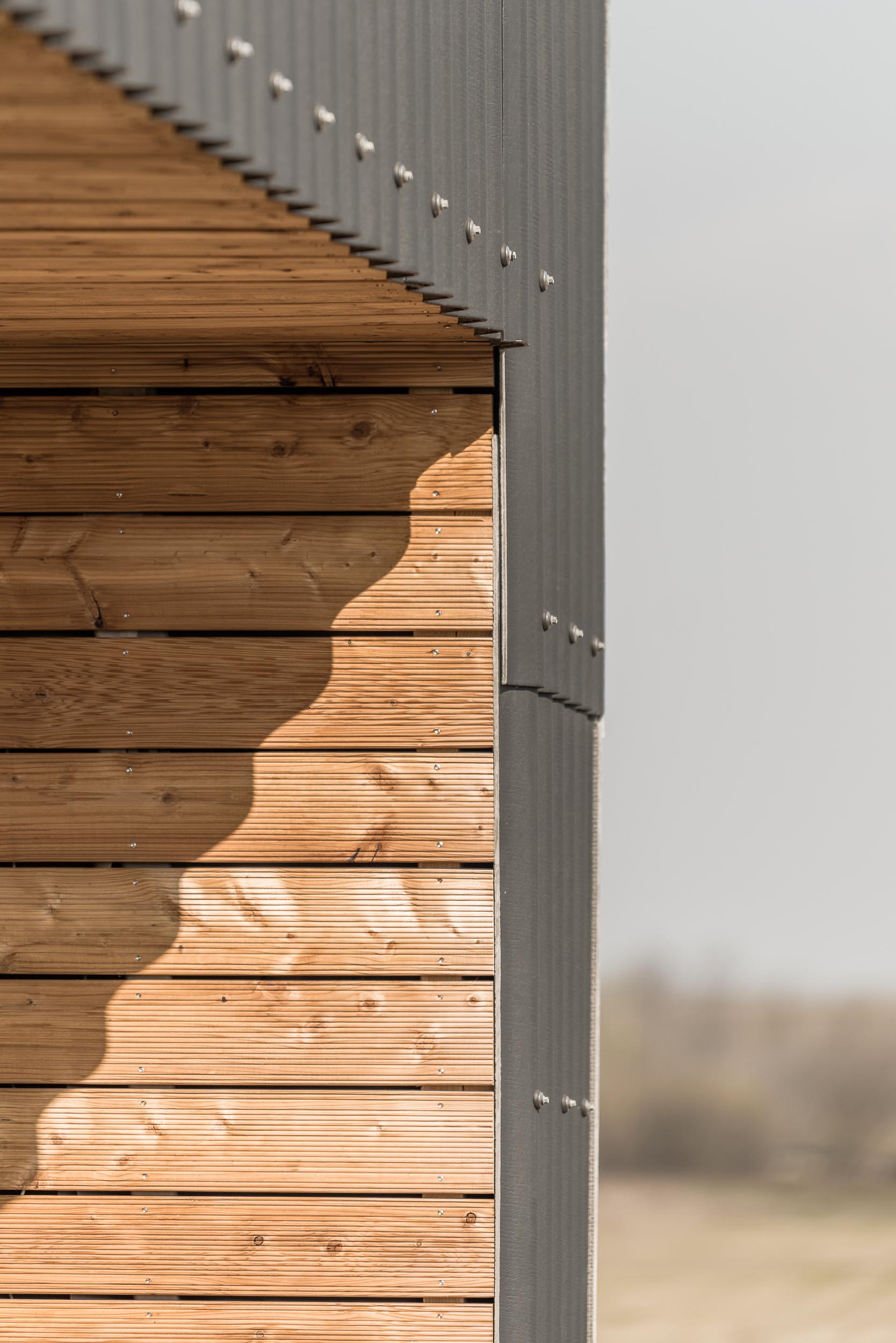 A modern black house with corrugated fibre-cement slate siding and alcoves lined with larch wood siding.