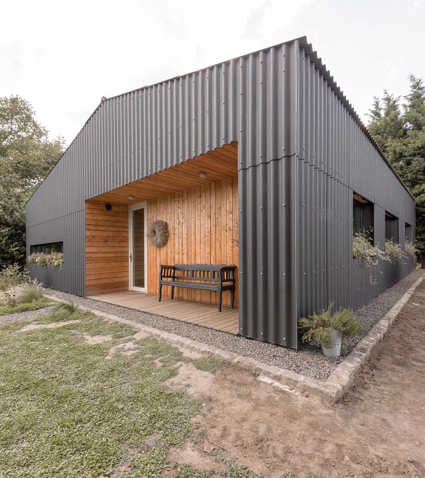 A modern black house with corrugated fibre-cement slate siding, black window frames, and wood lined alcoves.