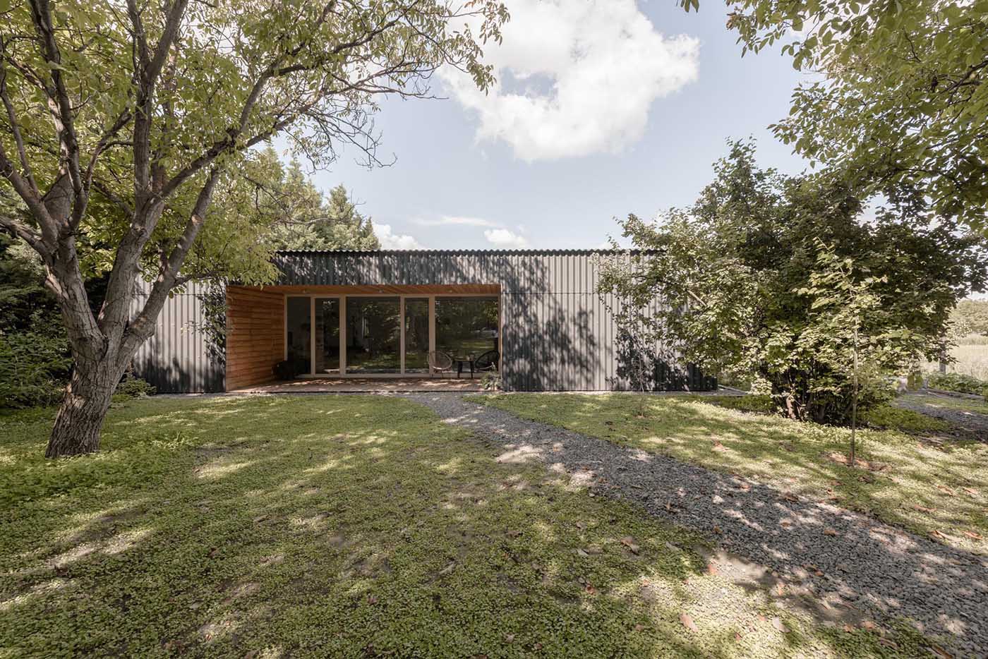 A modern black house with corrugated fibre-cement slate siding, black window frames, and wood lined alcoves.