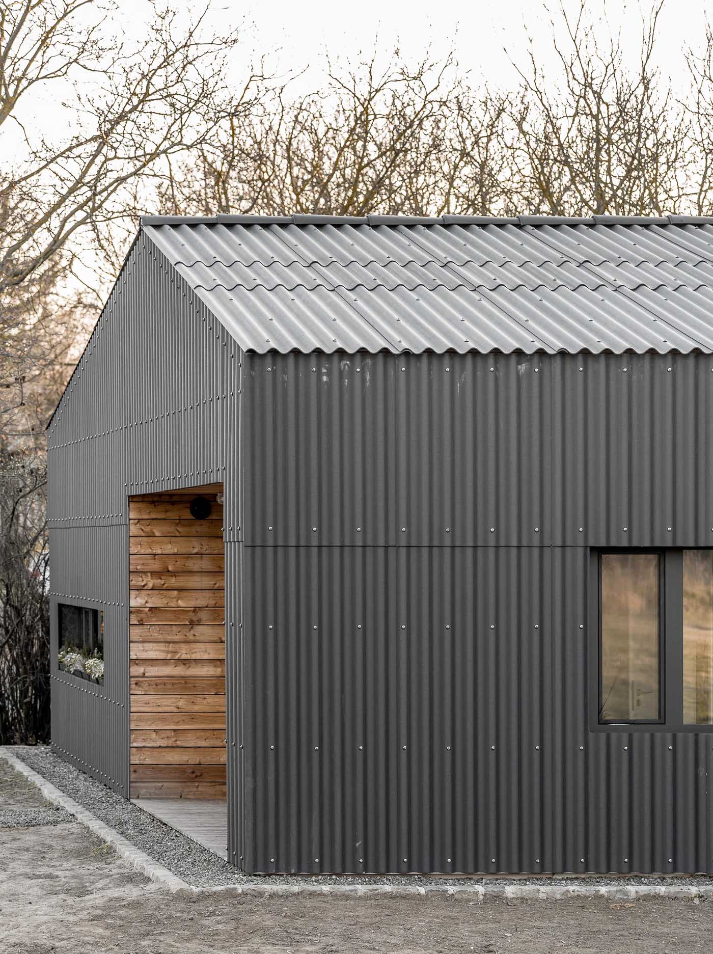 A modern black house with corrugated fibre-cement slate siding, black window frames, and wood lined alcoves.