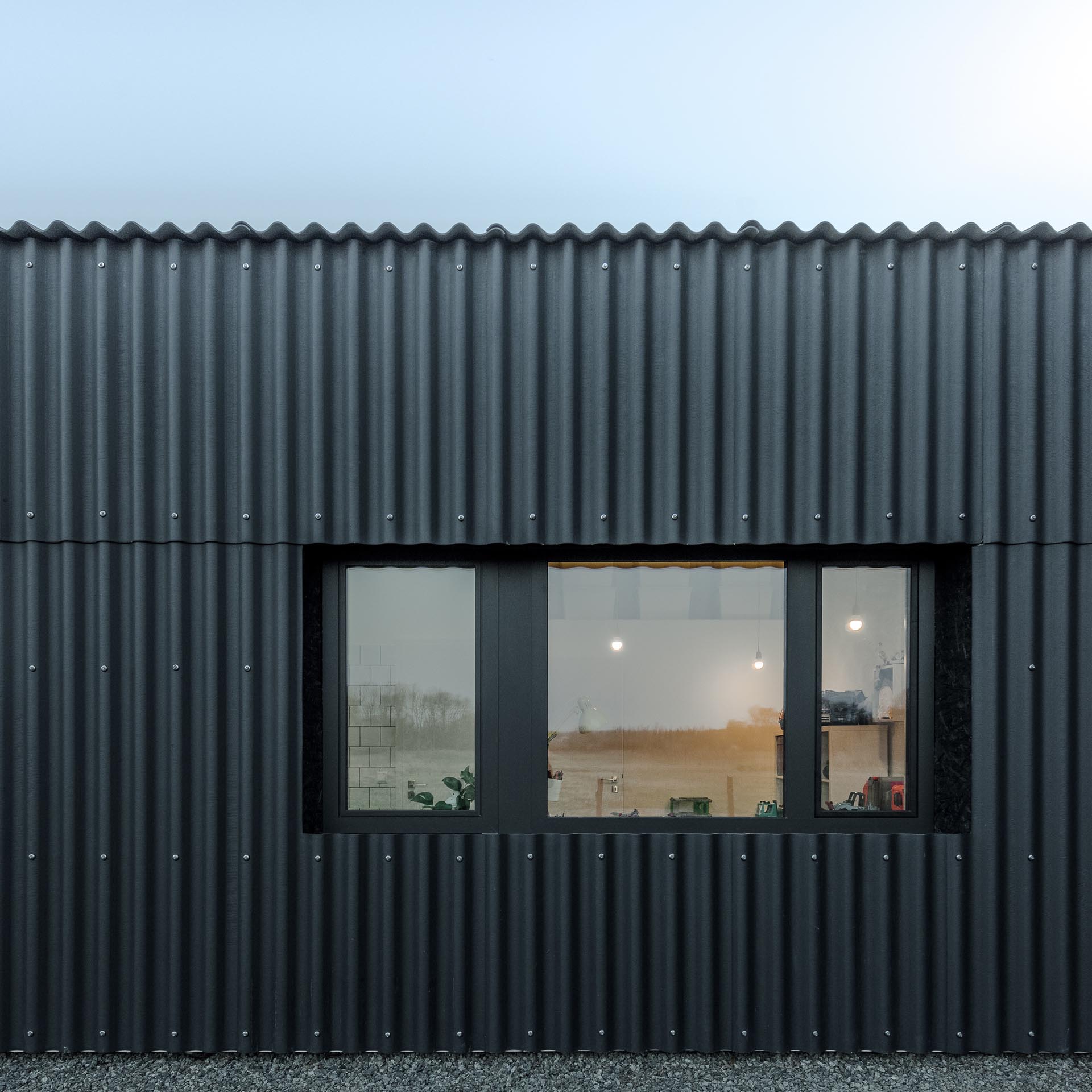 A modern black house with corrugated fibre-cement slate siding and black window frames.