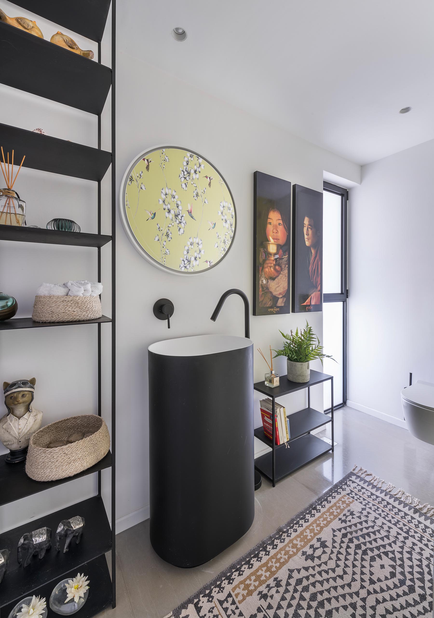 A powder room with a minimalist pedestal sink, black shelving, and a colorful yellow wallpaper with flowers and hummingbirds.