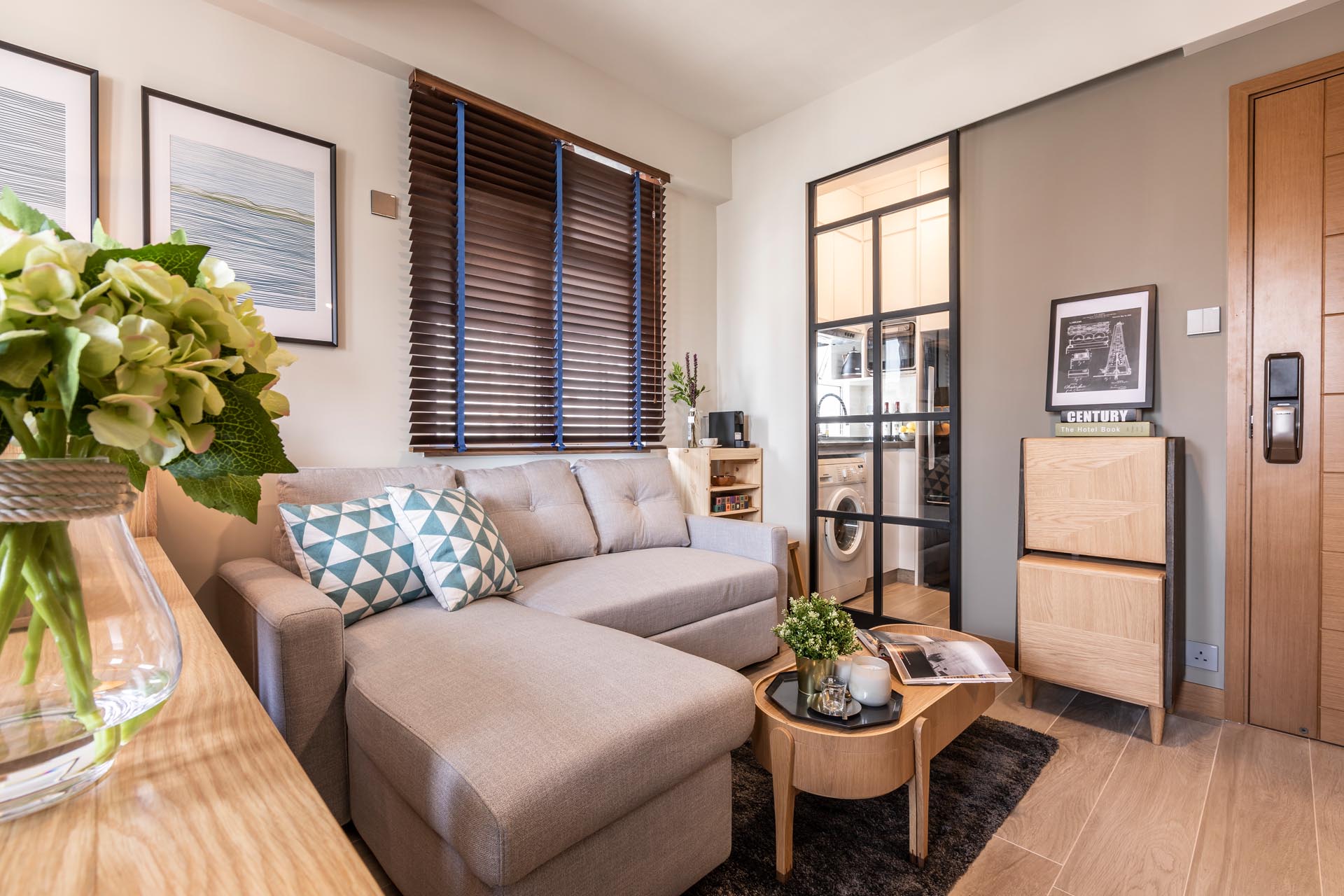 A small apartment with sleek charcoal black painted metal framed glass sliding door that reveals a tiny kitchen, that also includes a washing machine.