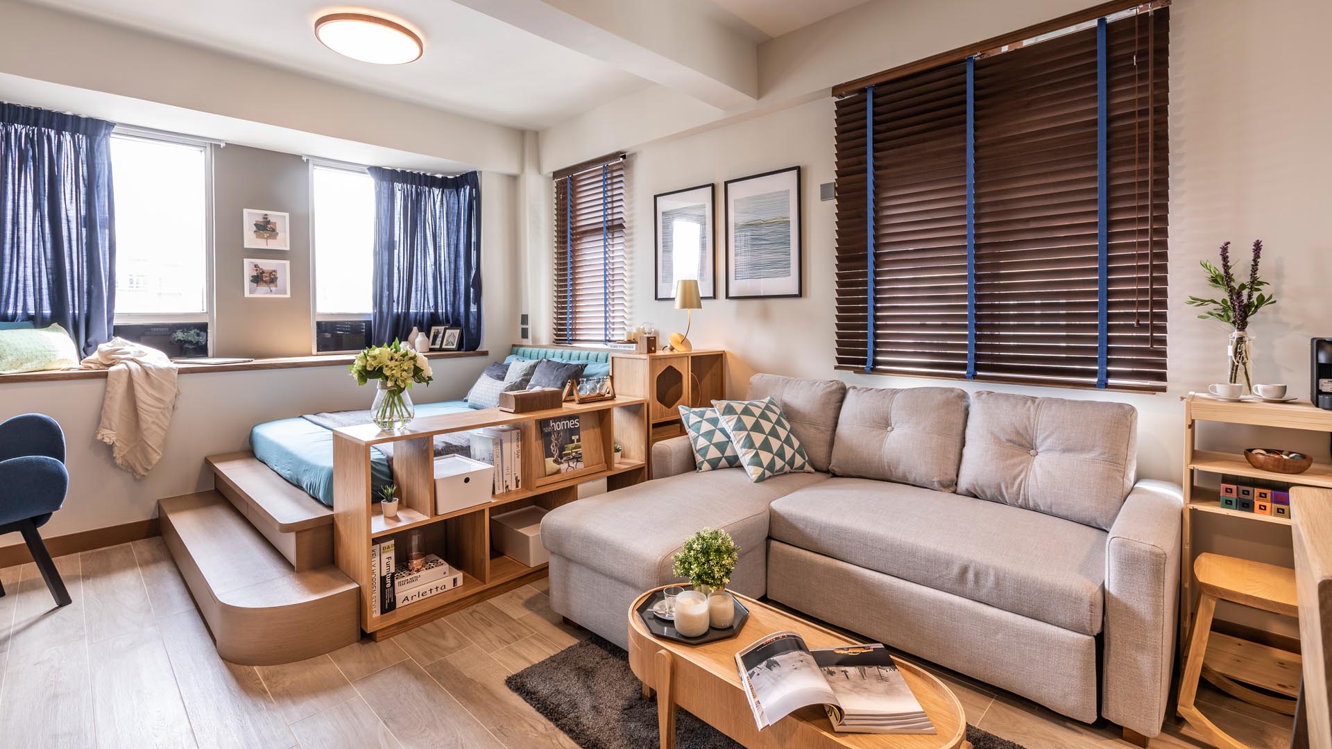 A small and modern apartment with a platform bed, a tiny kitchen, and a wood feature wall that hides a wardrobe, bathroom door, and structural column.