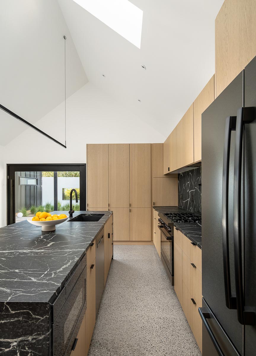 A modern kitchen with white oak cabinets includes black appliances and dark soapstone countertops