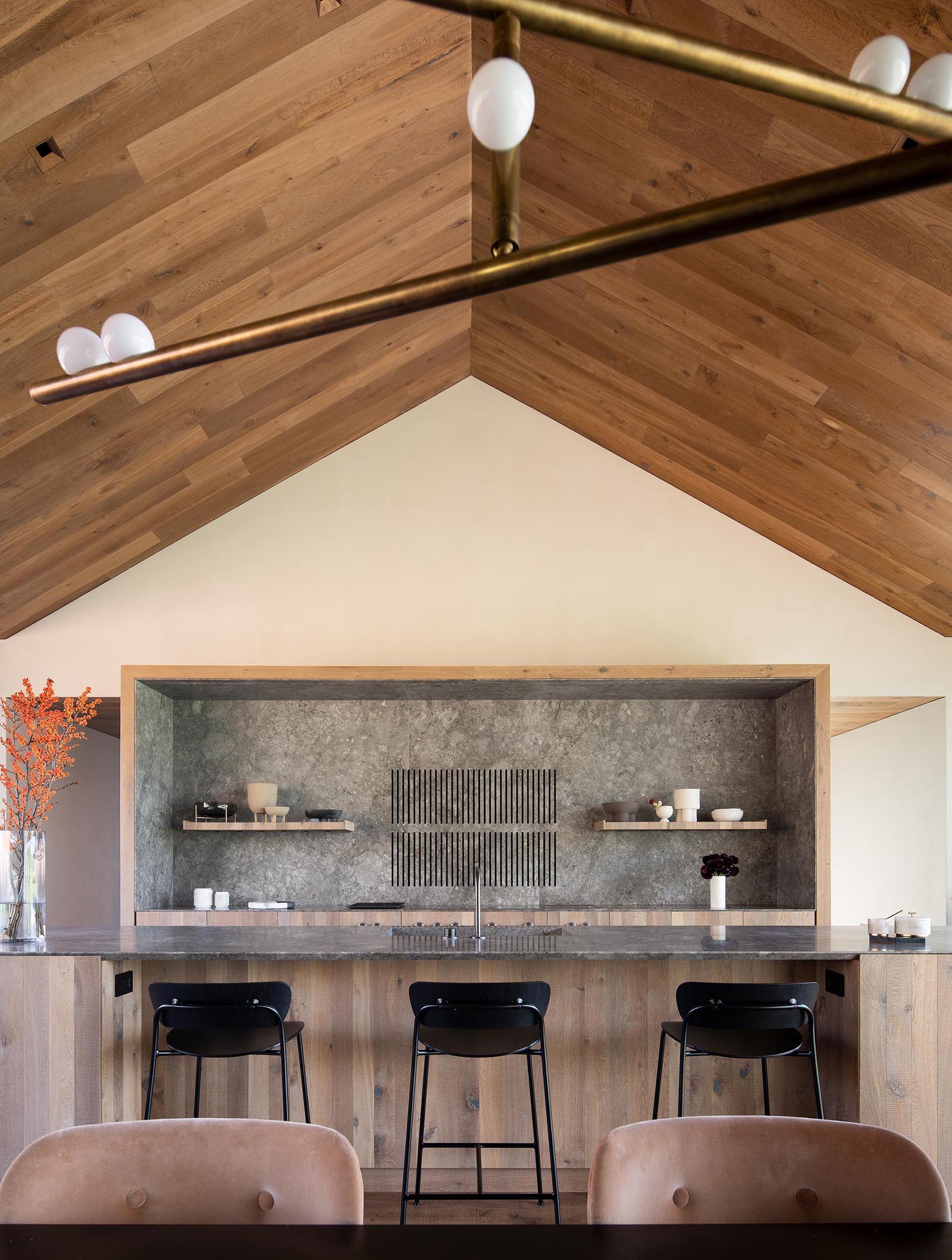 The steep roof pitches allow for high ceilings, while in the kitchen, a gray stone countertop and backsplash complement the light wood cabinets and island.
