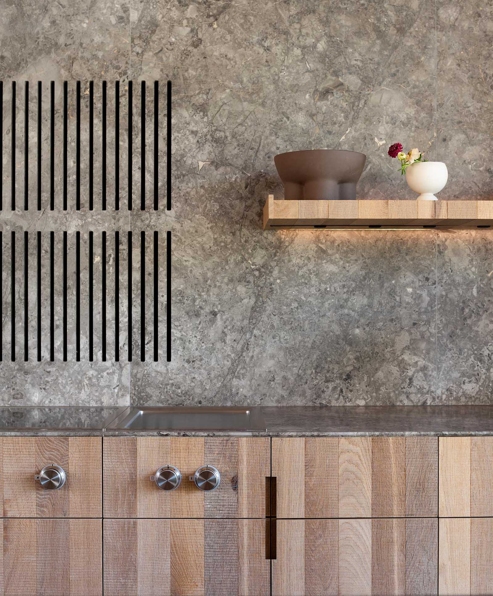 A modern kitchen with a gray stone countertop and backsplash that complements the light wood cabinets and island.