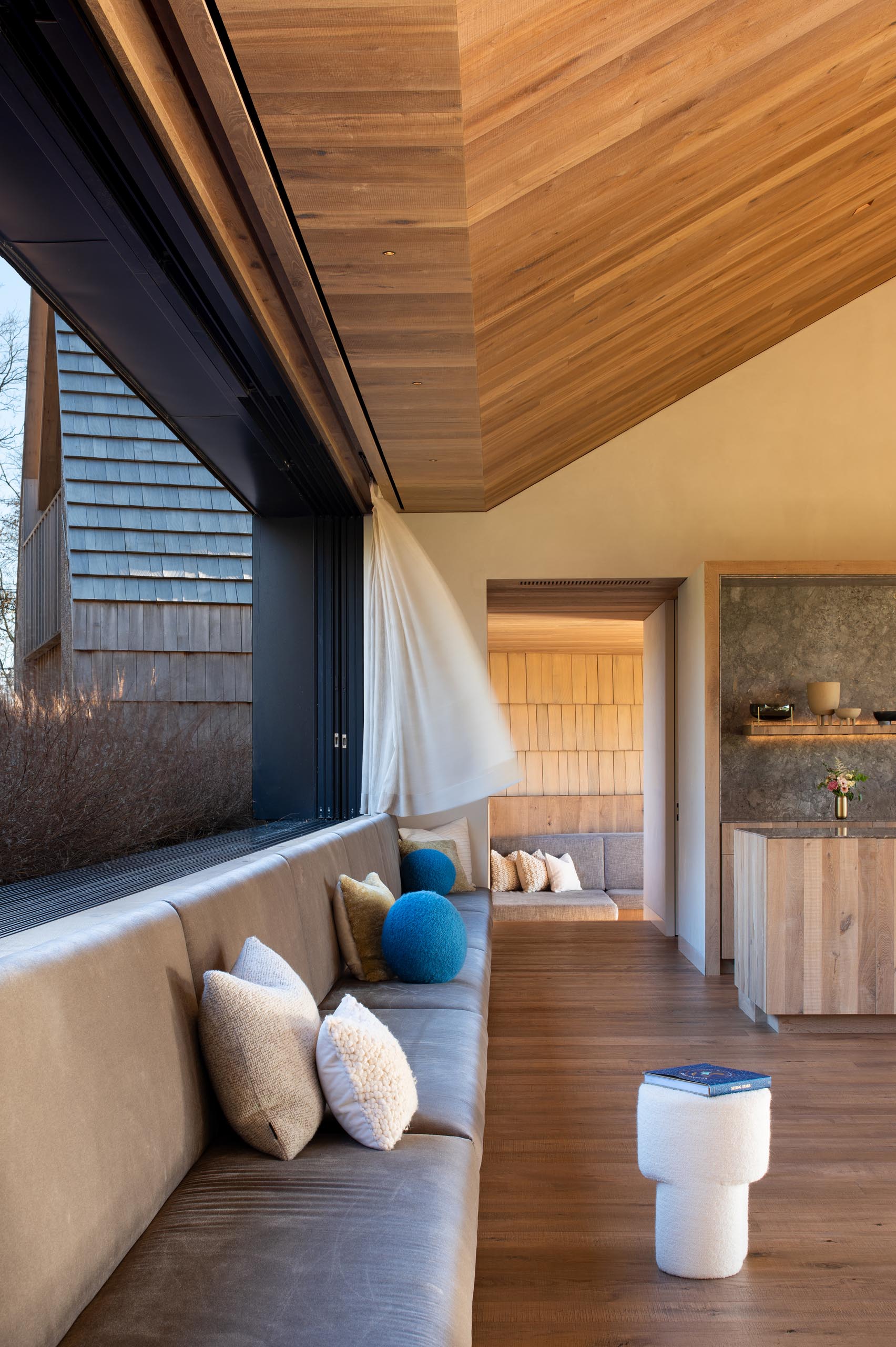Black window frames contrast the oak interior, while a long built-in bench adds ample seating to the open plan room that connects to the outdoor living room.