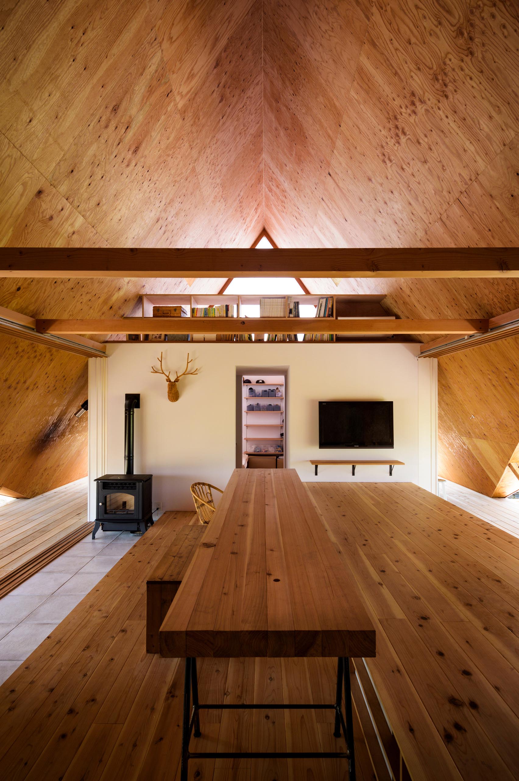 The wood-lined interior of this modern A-frame house has had its storage, partitions, and private rooms removed as much as possible in order to simulate one large open space that adapts to the user’s needs.