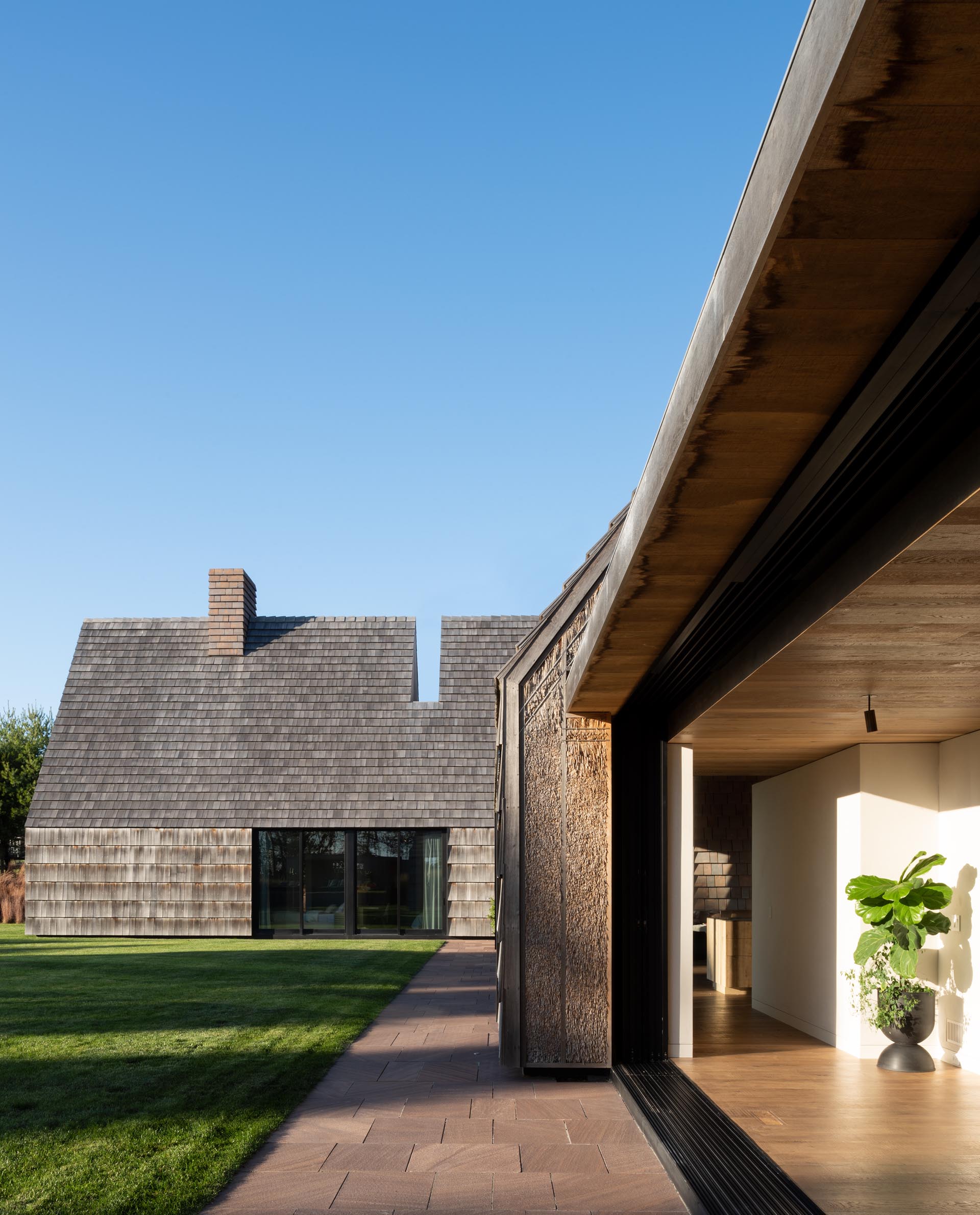 The weathered wood shingle siding that covers this modern home, while the traditional thatch siding is packed neatly between the exposed exterior framing and makes reference to the grasses of the pasture.