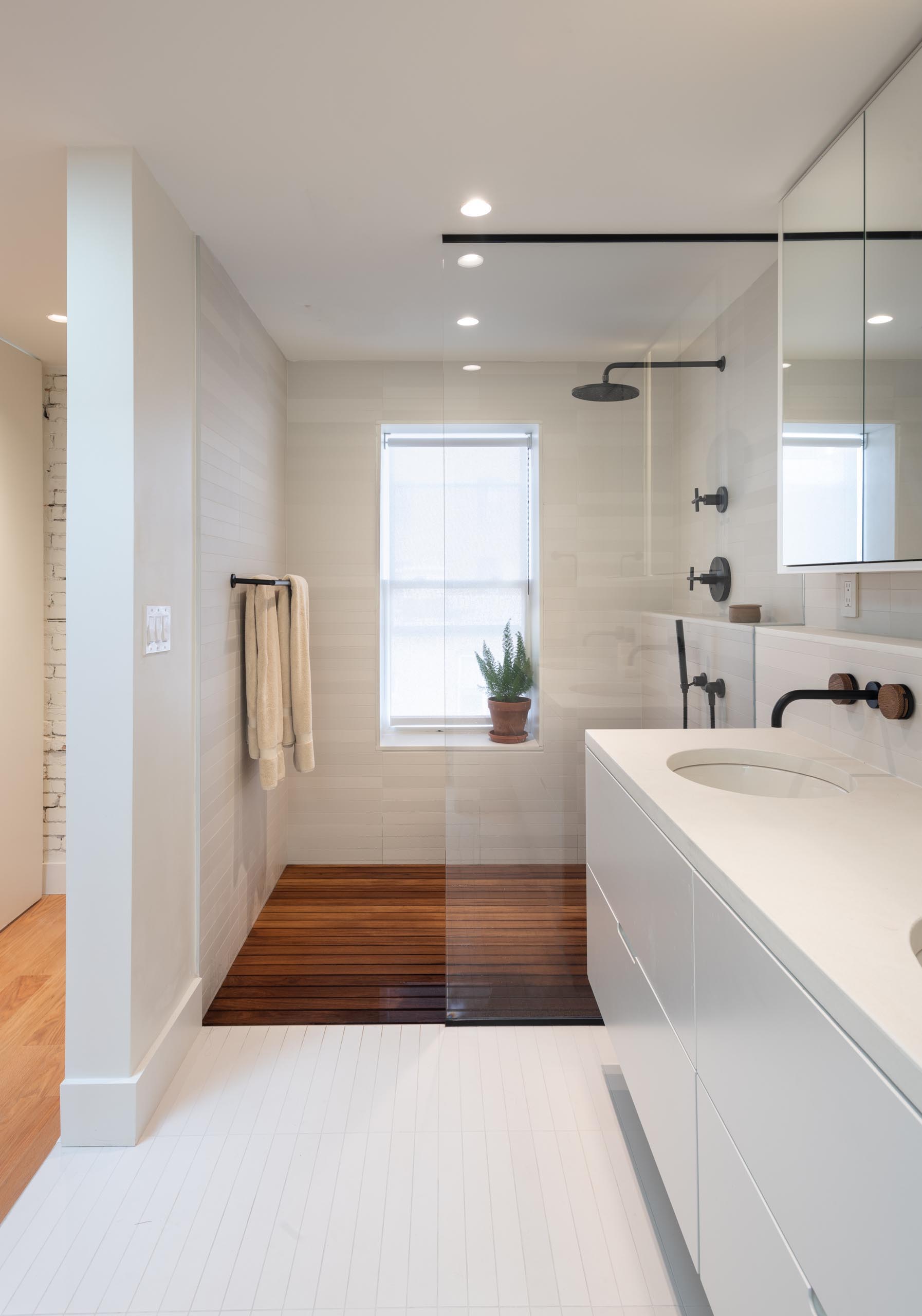 A modern bathroom with a floating white vanity, a walk-in shower with wood floor, and black accents.
