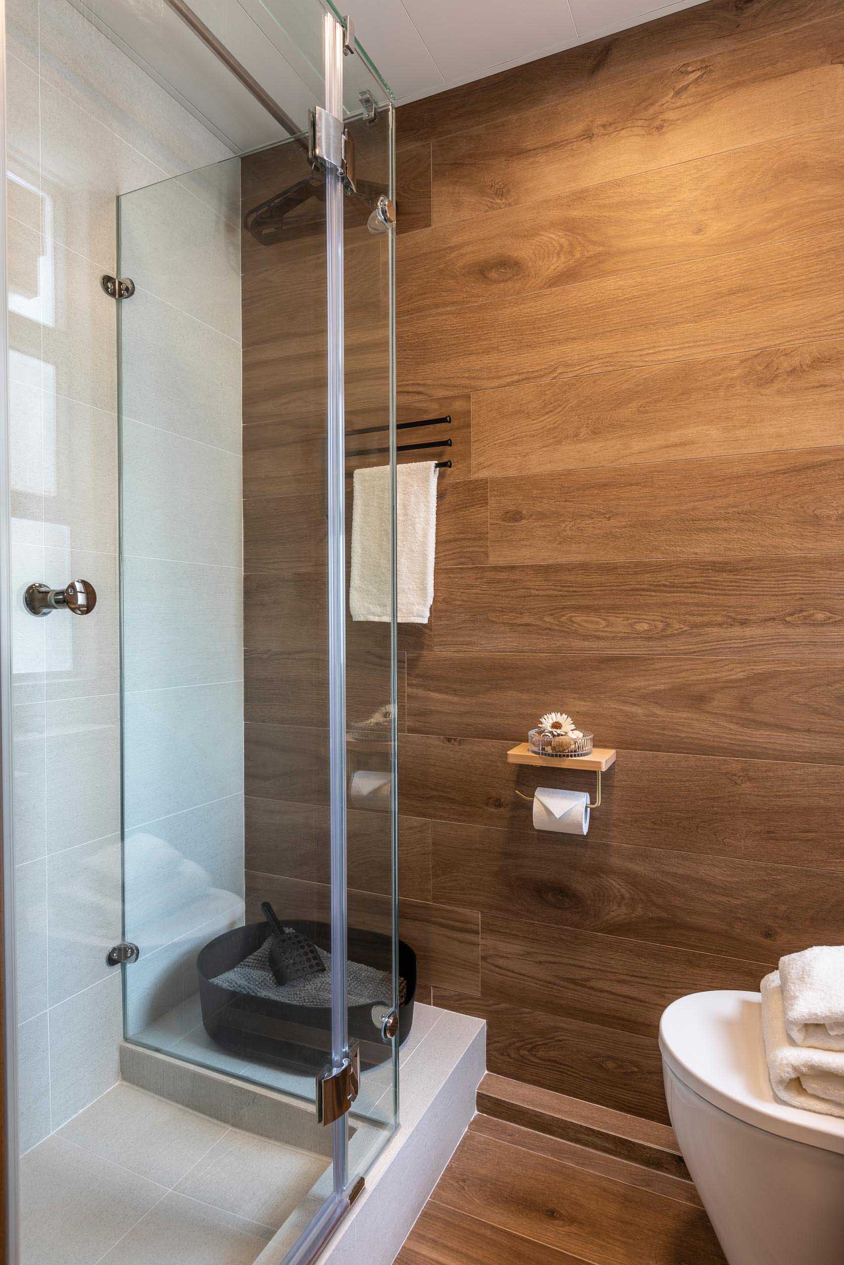 This modern bathroom in a small apartment includes a wood accent wall and a glass-enclosed shower.