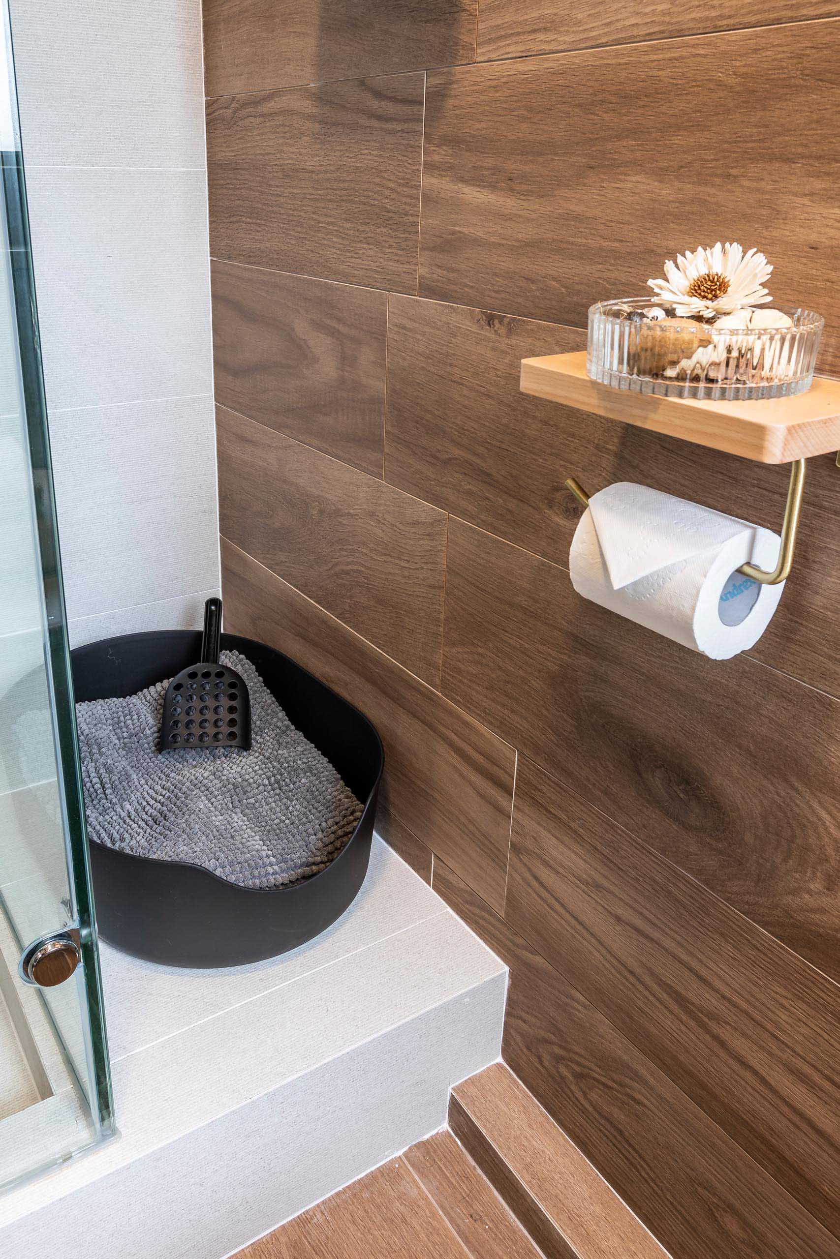 This modern bathroom in a small apartment includes a wood accent wall and a glass-enclosed shower.