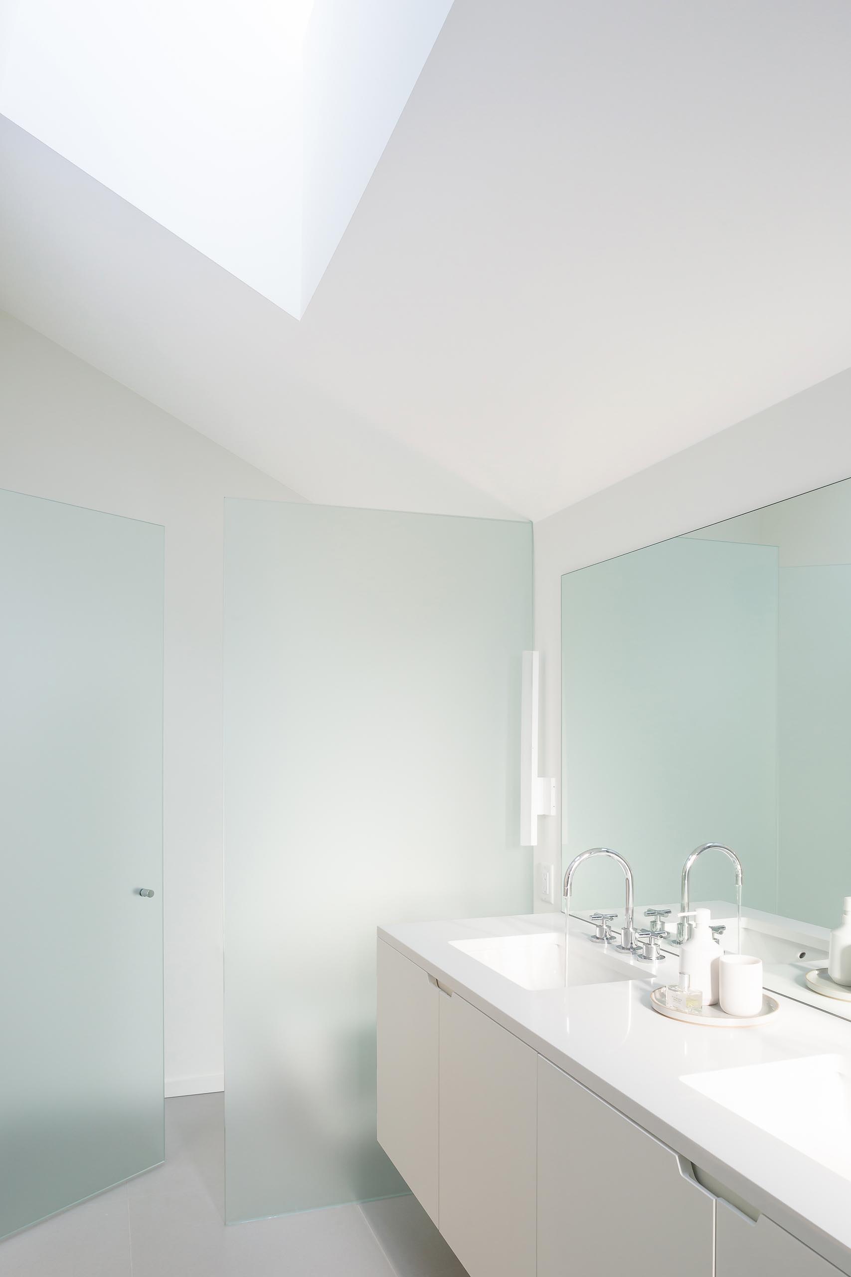In this modern bathroom, there's a minimalist white vanity, a skylight, and a shower hidden behind frosted glass.