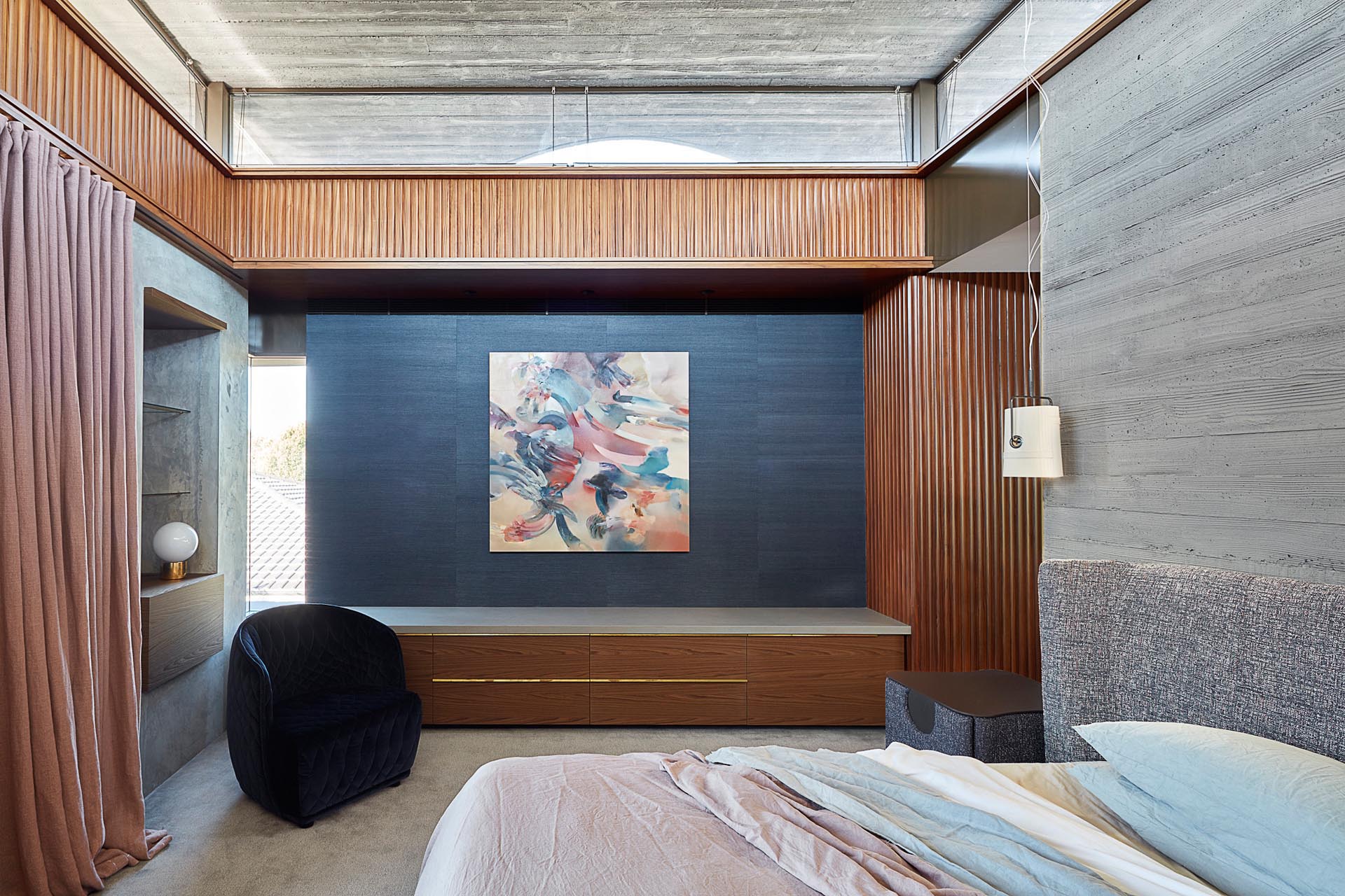 A modern master bedroom with a built-in bench, and board formed concrete walls.