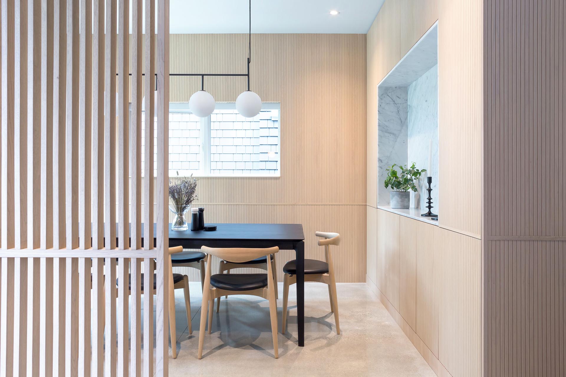 Wood clad interiors made from Tambour oak veneer, like in this modern dining room, add a sense of warmth to the home, while the floors are polished concrete.