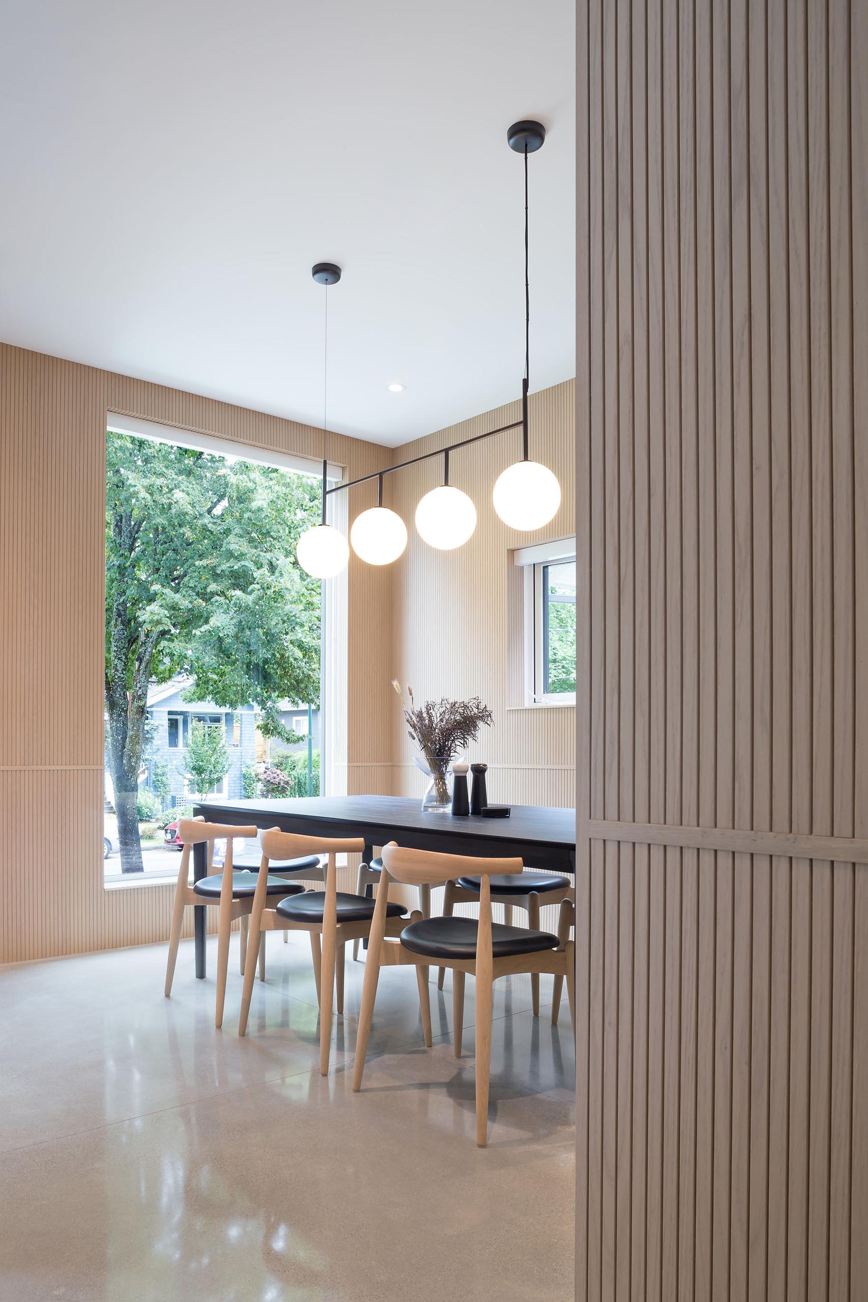 Wood clad interiors made from Tambour oak veneer, like in this modern dining room, add a sense of warmth to the home, while the floors are polished concrete.